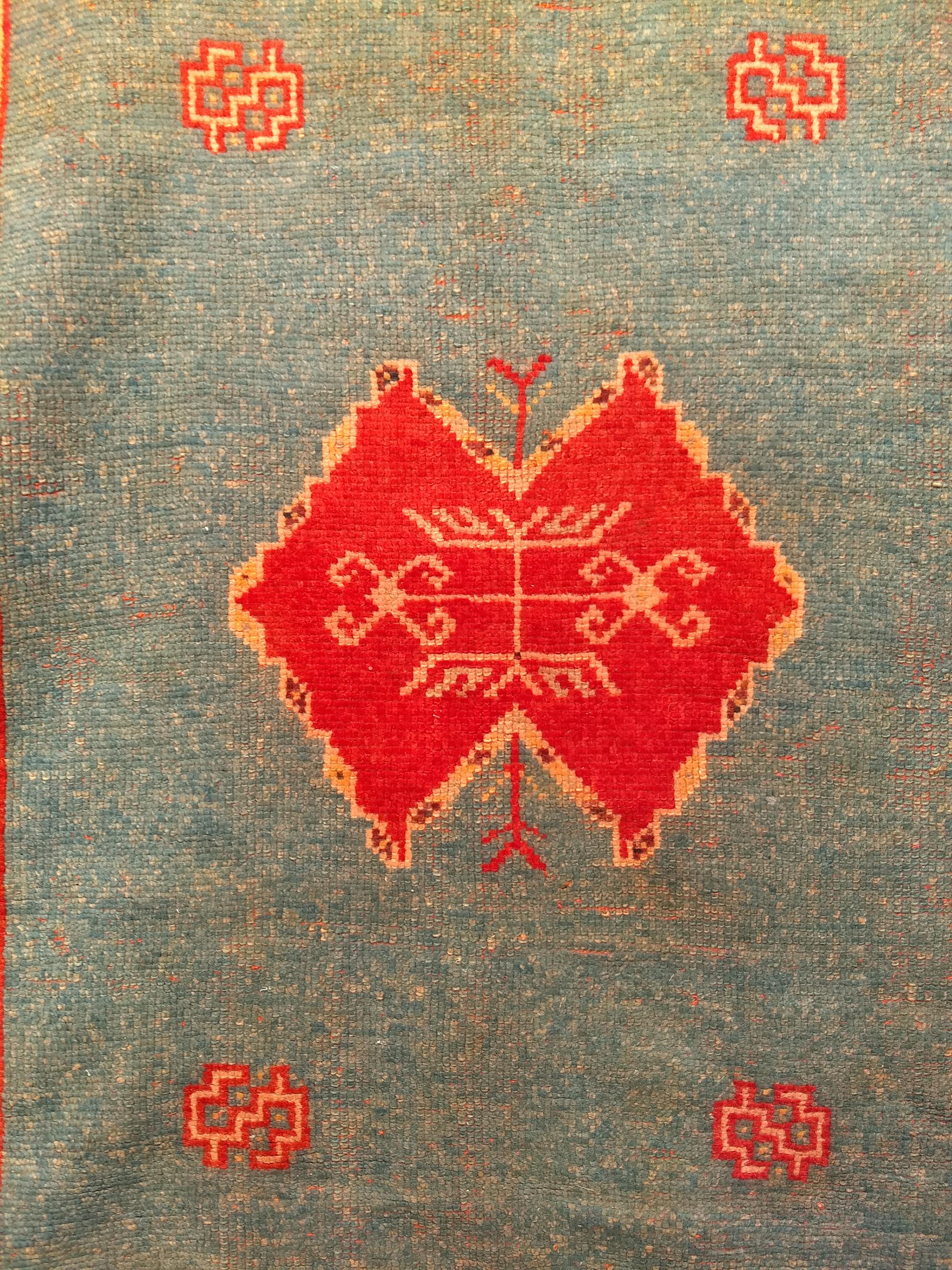 Tapis marocain vintage à motif géométrique ouvert dans un champ vert abrash (variation de couleur) avec un petit médaillon rouge et jaune et des écoinçons rouges.  Le tapis présente une magnifique bordure jaune safran avec des motifs rouges, verts