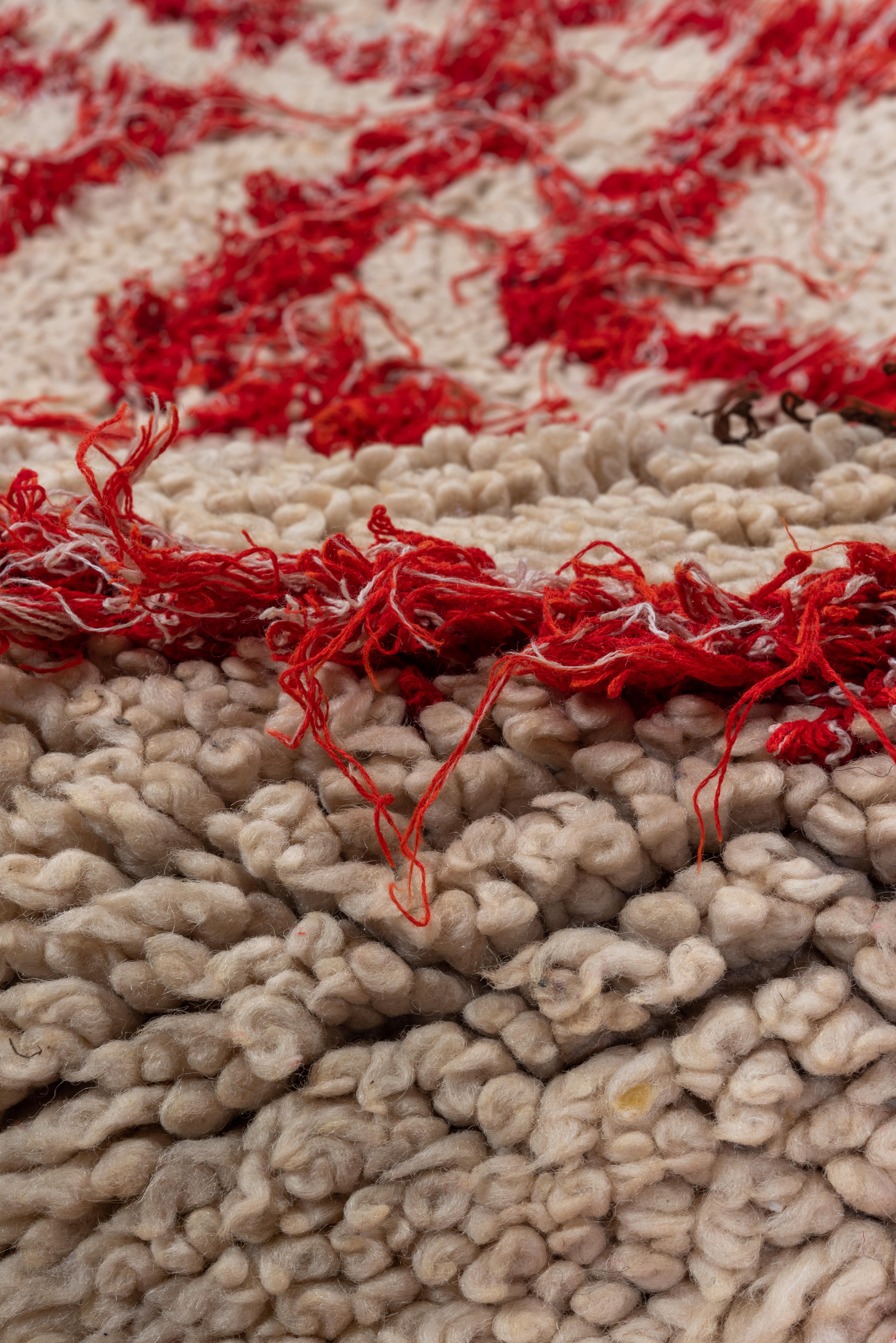 Esta diminuta alfombra marroquí vintage cautiva con su atrevido y anguloso diseño en zigzag de color rojo carmesí, dramáticamente perfilado con toques de marrón espresso sobre un suave campo marfil. Las líneas irregulares, dibujadas a mano, hablan