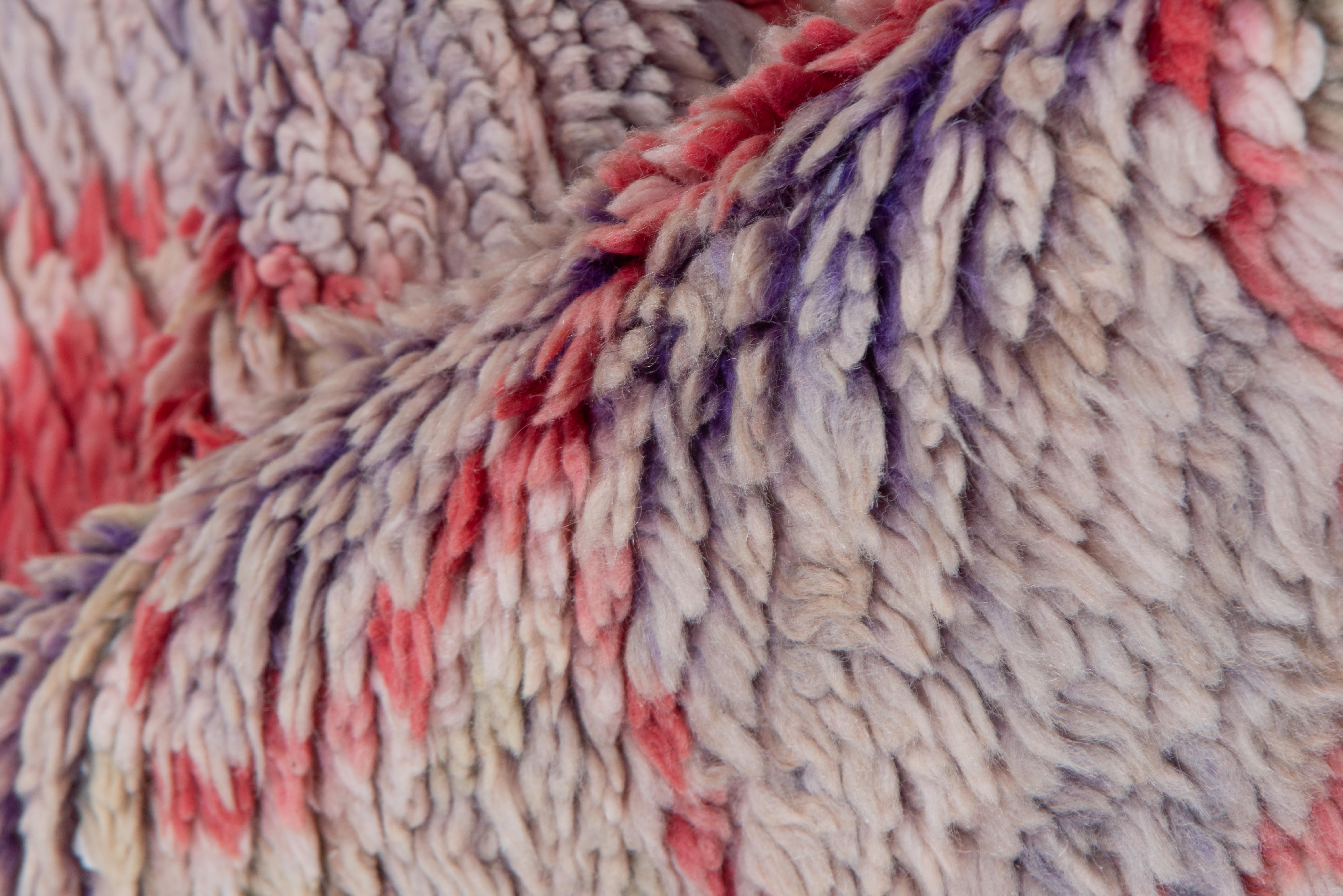 Esta alfombra vintage, un vibrante ejemplo del arte textil marroquí, muestra un rítmico diseño de celosía de rombos en lila suave y carmesí saturado, con suaves toques de rubor y marfil. La interacción de tonos fríos y cálidos crea un seductor