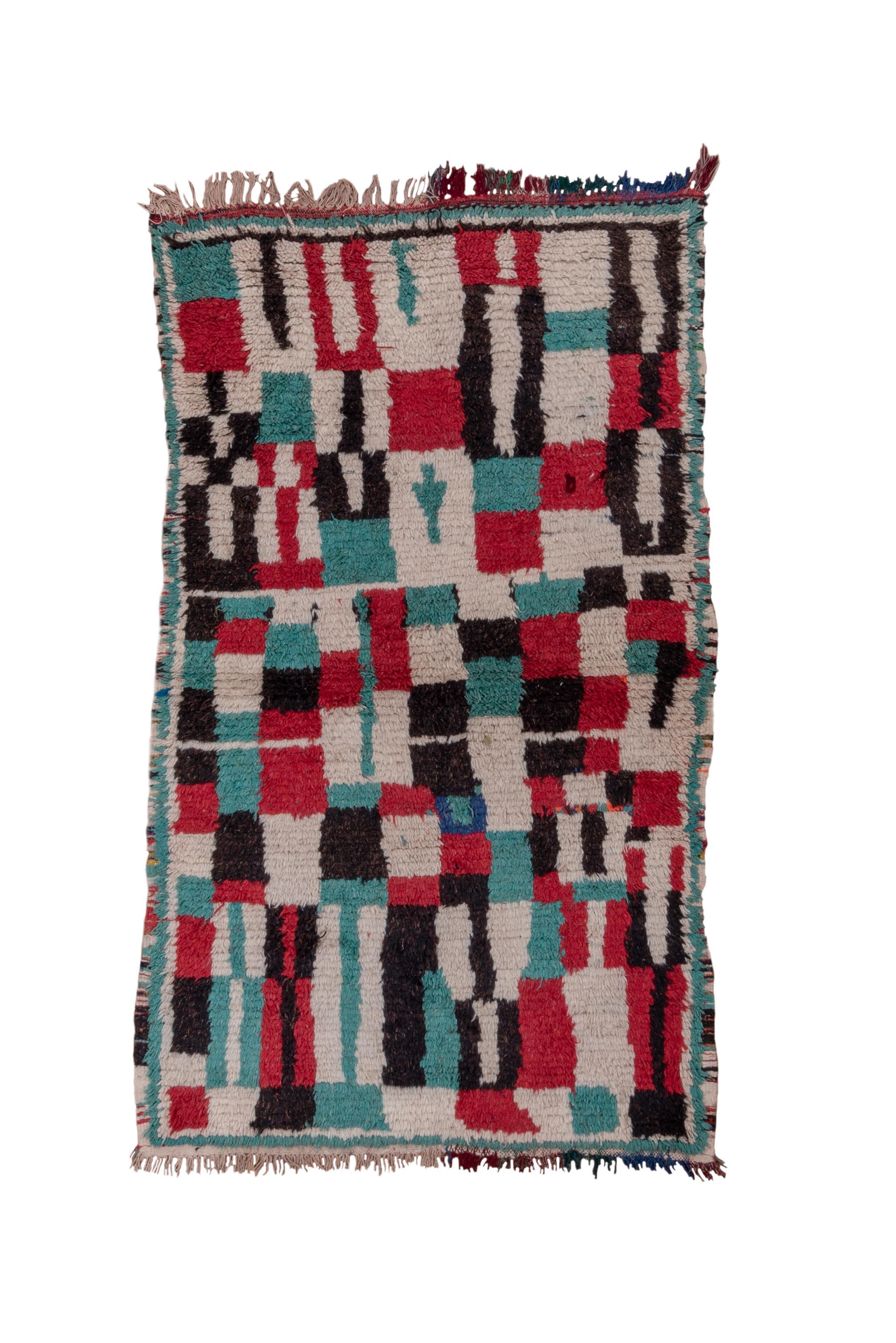 Esta alfombra vintage, un ejemplo visualmente cautivador del arte marroquí, presenta un diseño abstracto en damero compuesto por bloques irregulares en verde azulado, carmesí, negro y marfil. El motivo palpita con energía dinámica, evocando la