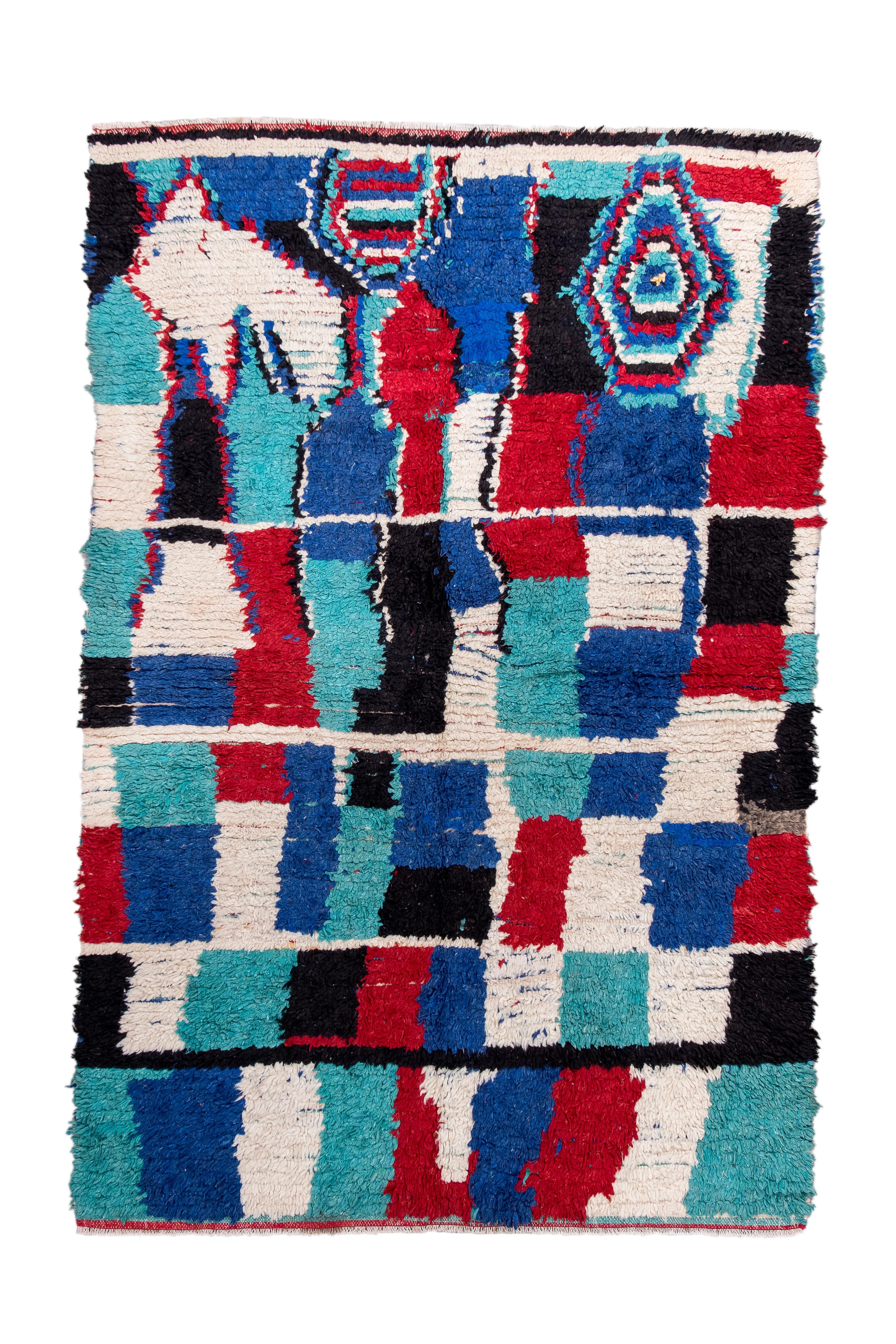 Esta alfombra vintage, sorprendente ejemplo de la narrativa visual marroquí, deslumbra con una enérgica interacción de tonos saturados -azul cobalto, carmesí, aguamarina, marfil y negro intenso- dispuestos en una composición rítmica, casi cubista.