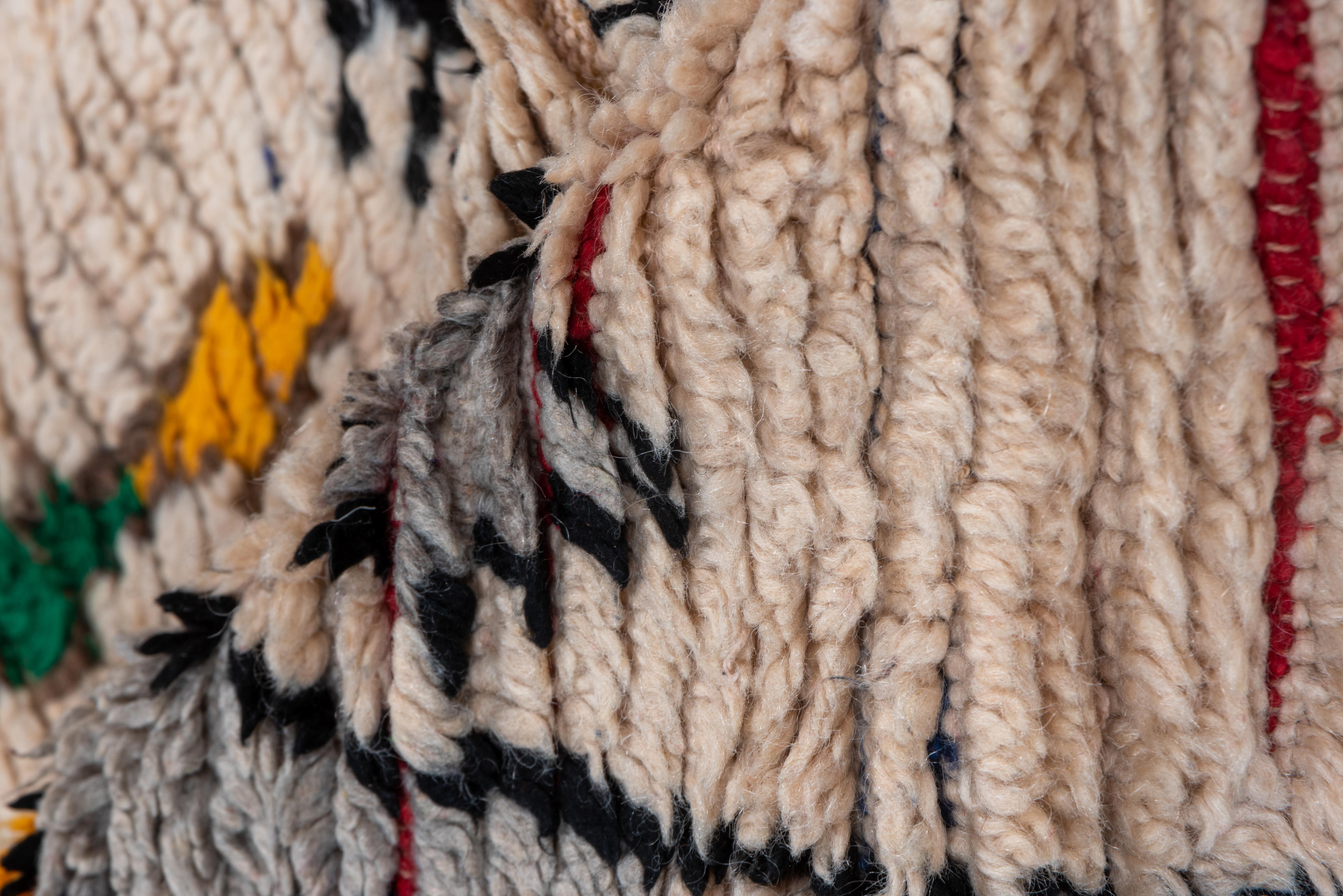 Dieser farbenfrohe marokkanische Vintage-Teppich zeigt ein cremefarbenes Feld, das durch kühne Stammesmotive und verspielte Farbakzente belebt wird. In der Mitte befindet sich ein dynamisches Stufenmedaillon in Schwarz, Rot und Gelb, flankiert von