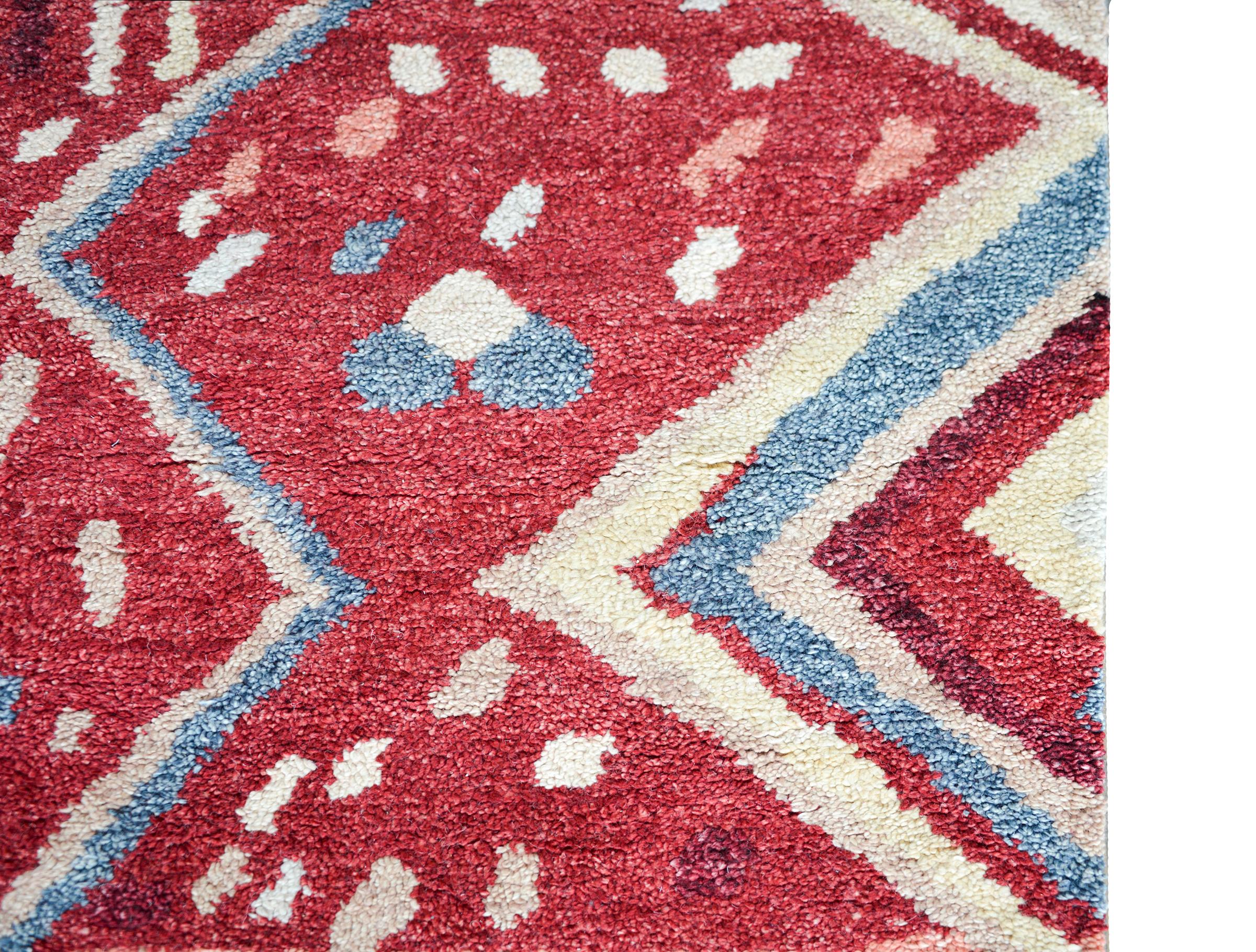 A beautiful Moroccan rug with a modernist geometric pattern containing multiple light indigo and white zigzag stripes against a light and dark cranberry background with more geometric patterns.