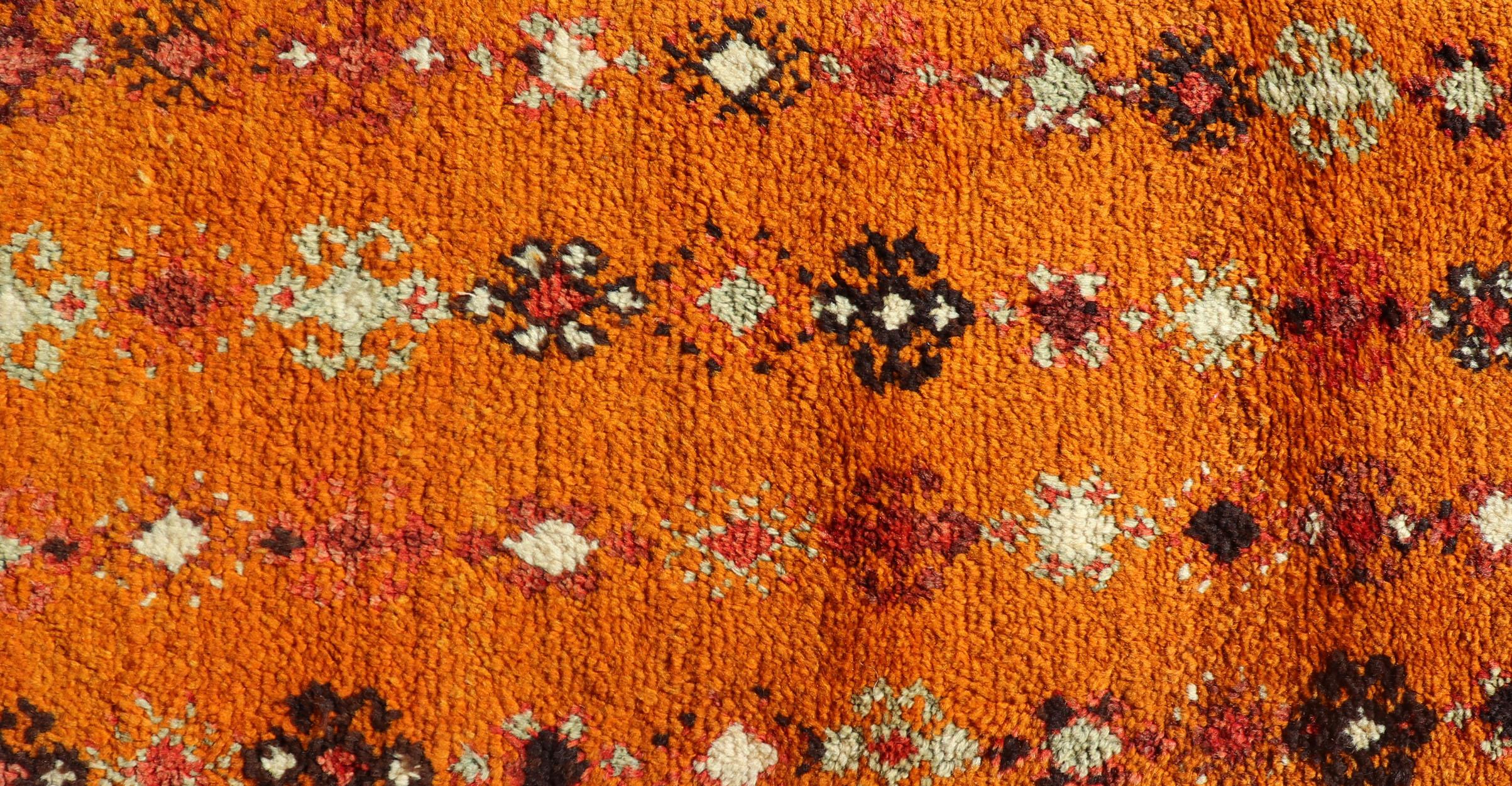 This lovely Vintage Moroccan carpet (circa 1940s), features an all-over sub-geometric design rendered in Saffron, Ivory, Brown and variations of Red, Green, Gold & Orange. These unique combination of colors and motifs render this rug into a