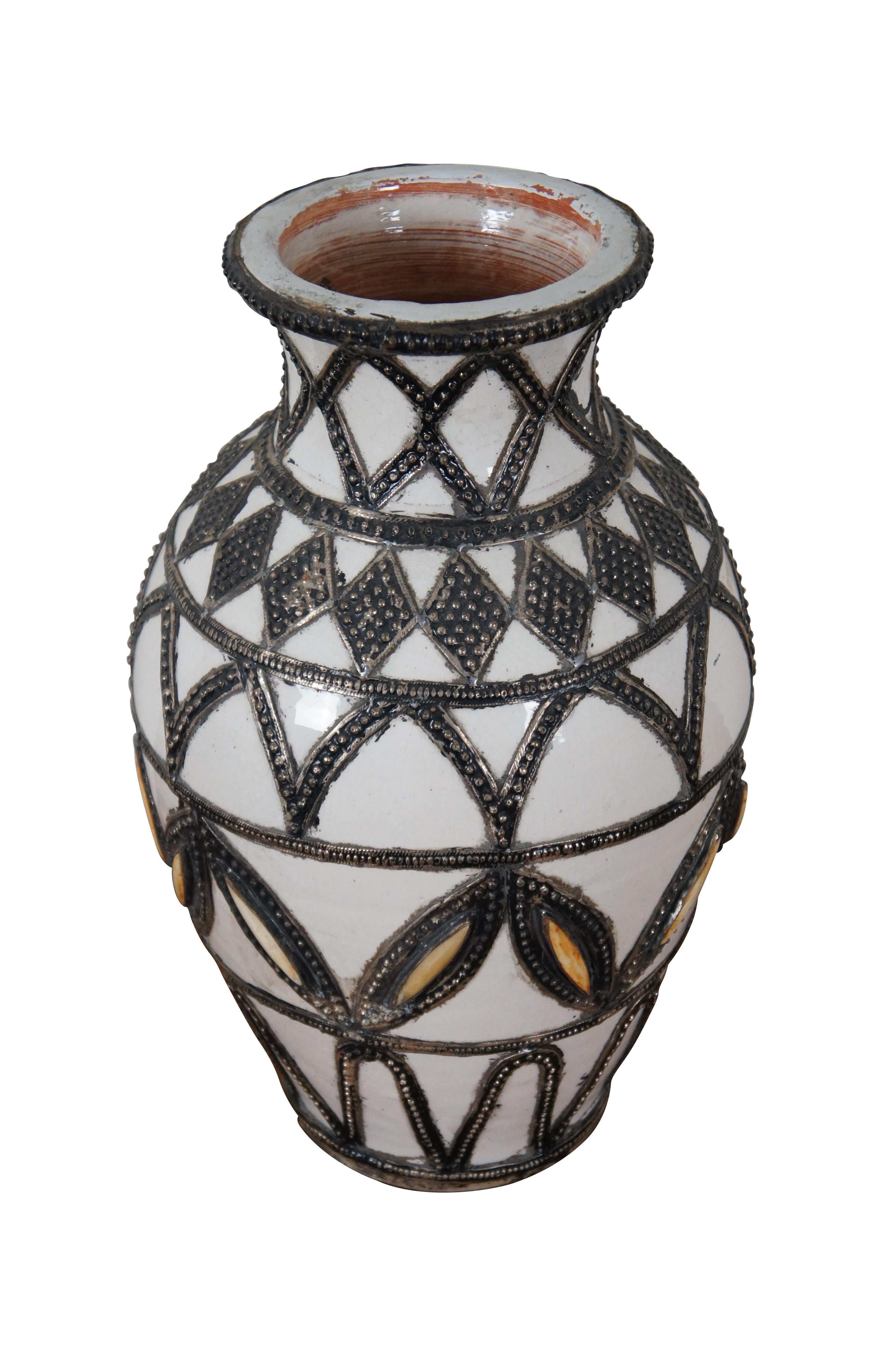 A large and impressive Moroccan ceramic vase, glazed in white with a variety of geometric inlaid studded nickel-silver designs.

Dimensions:
10” x 16.5” (Diameter x Height)