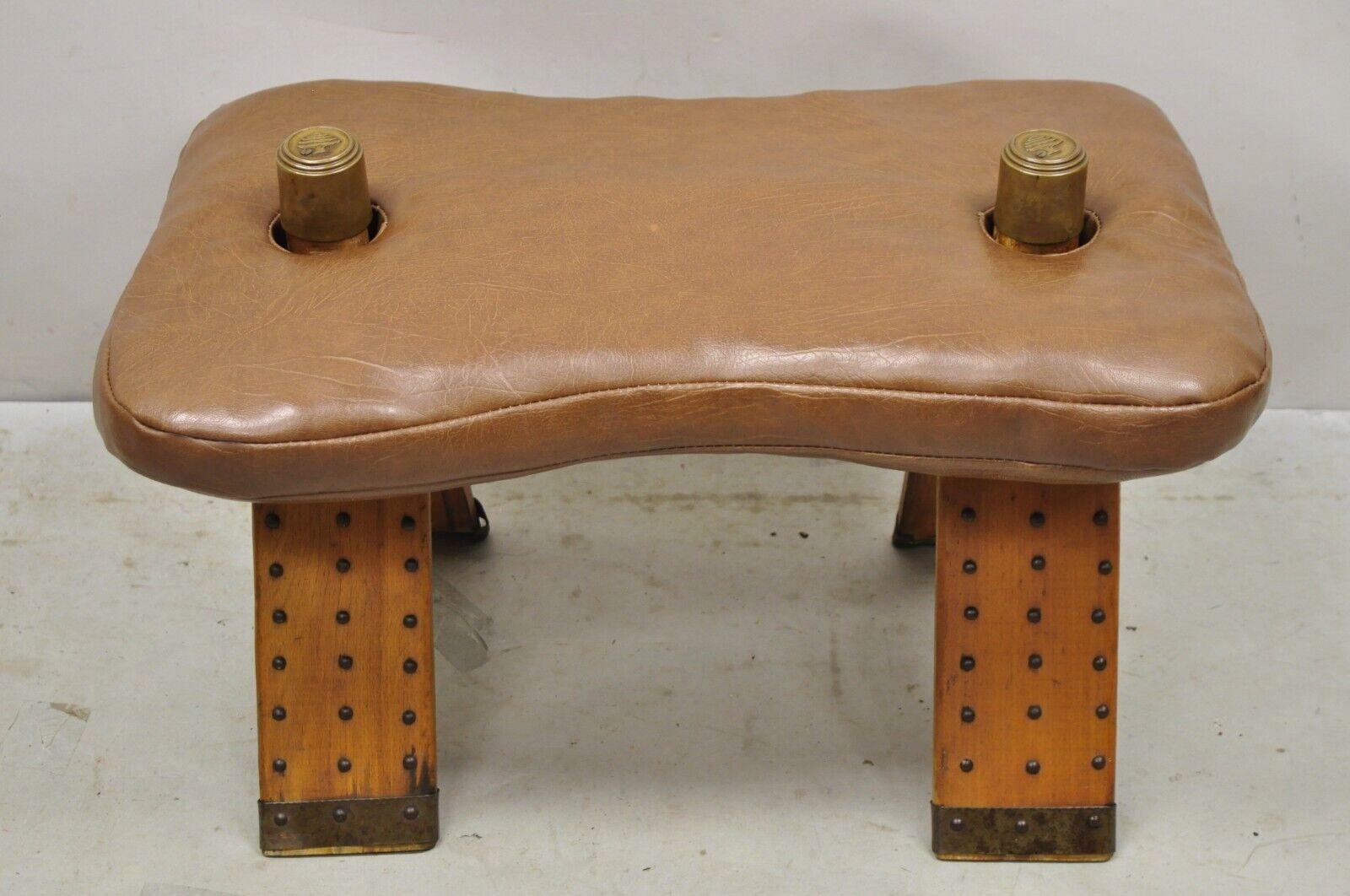 Vintage Moroccan Style Brown Vinyl Wooden Camel Saddle Ottoman Stool. Item features Brown vinyl saddle cushion, brass accents, wooden base, very nice vintage item, great style and form. Circa Mid 20th Century. Measurements: 16