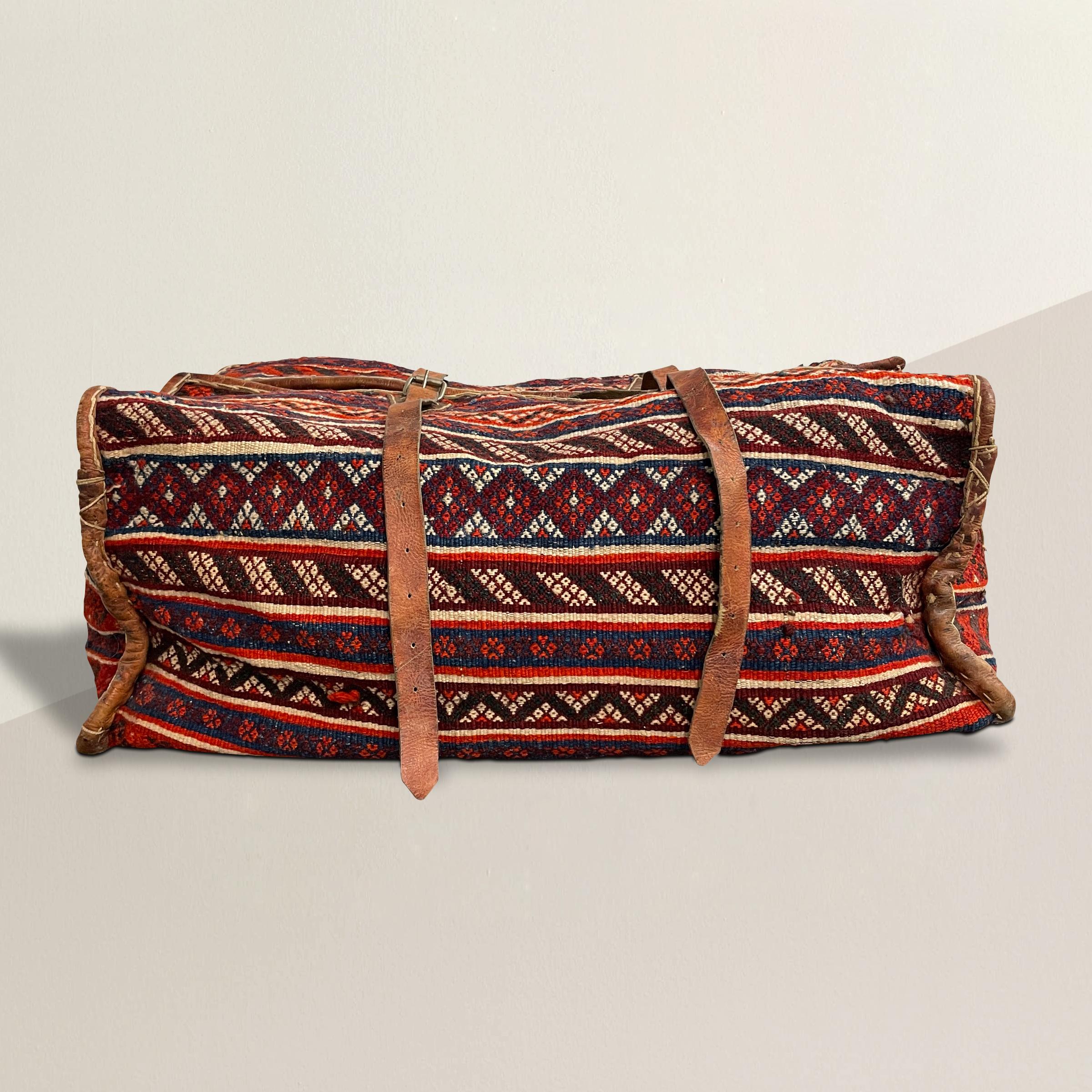 A striking 20th century Moroccan tent bag made from a vintage Kilim rug with myriad geometric patterns, and trimmed in leather with leather handles and straps with brass clasps. Perfect for storing blankets, pillows, or any myriad things you have