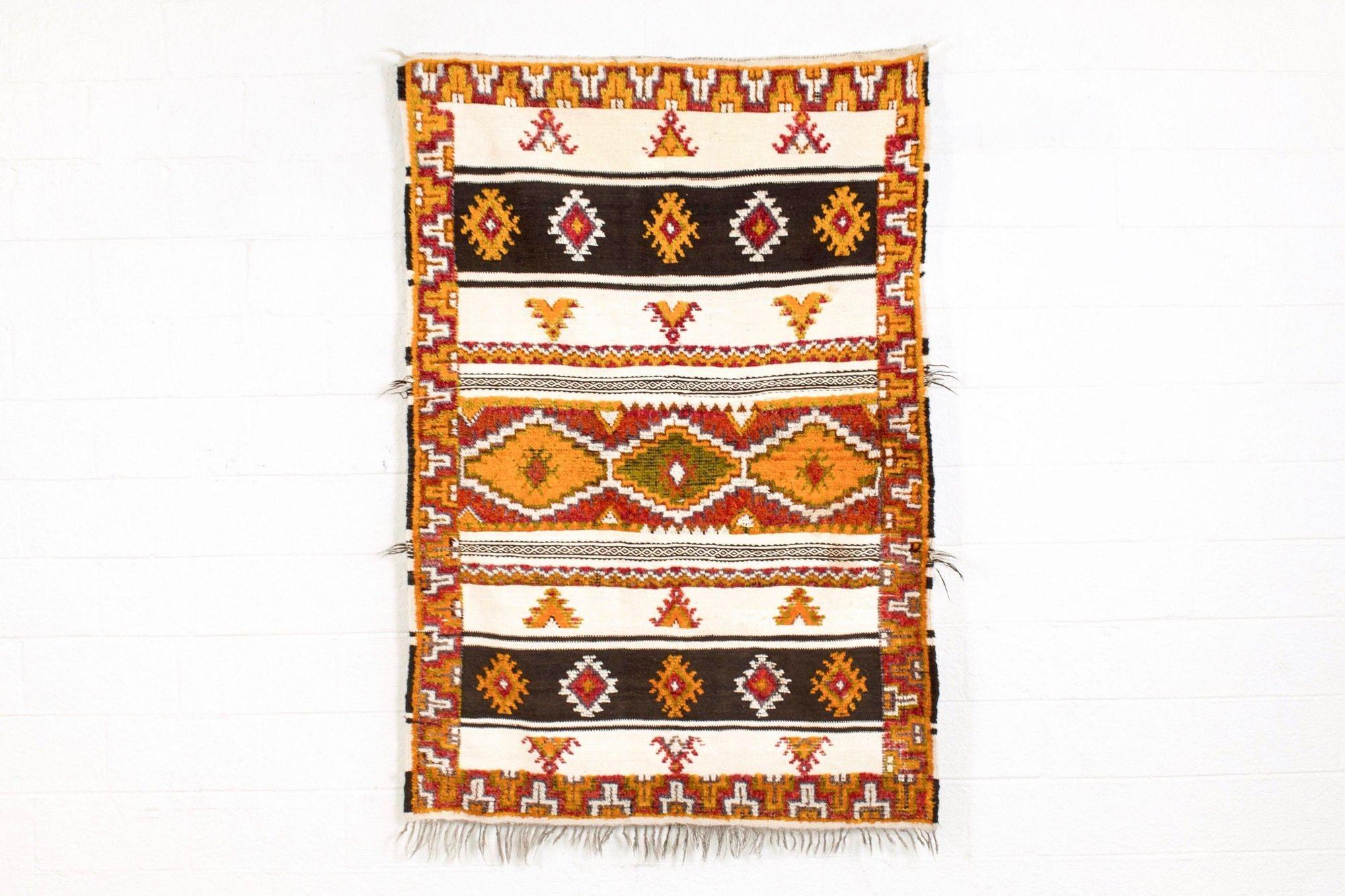 Questo bellissimo tappeto berbero marocchino vintage tessuto a mano risale alla metà del XX secolo. Presenta un disegno geometrico a bande simmetriche infuso di simbolismo tribale in splendide tonalità di arancione, rosso, rosa, verde, grigio,