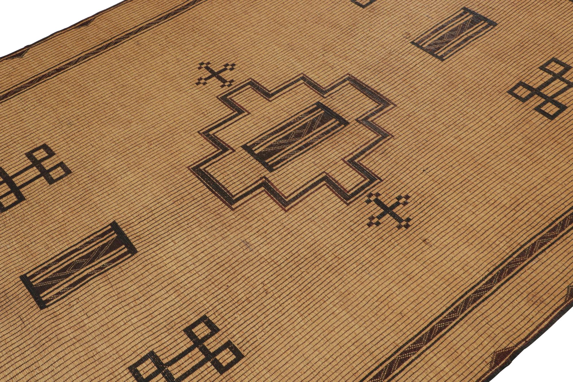 This vintage Moroccan floor covering is a 9x13 Tuareg mat from the nomadic tribe of the same name. Handwoven with reeds and leather circa 1950-1960, its natural materials enjoy warm beige, brown and black tones, with rich burgundy accents in its