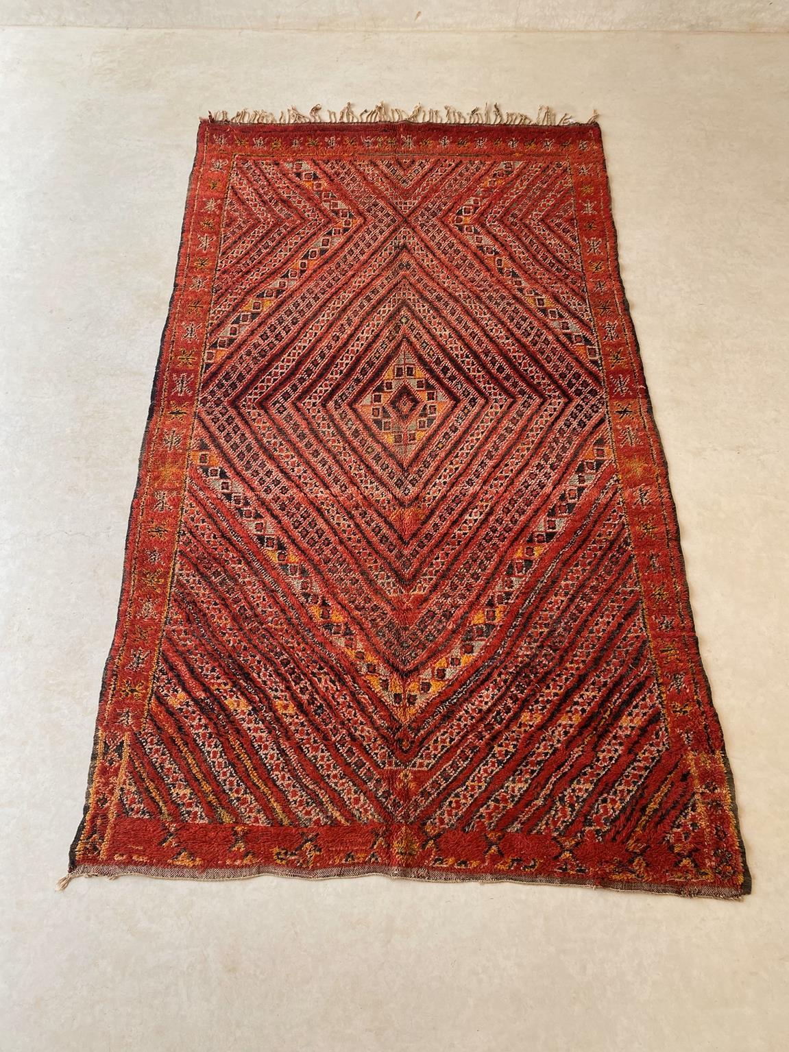 This beautiful vintage rug from the Zayane tribe is a great find! The main background color is a bright red with intricate designs in black, beige, yellow/orange and sage green. The pattern is a central, multiplied diamonds and the whole rug is