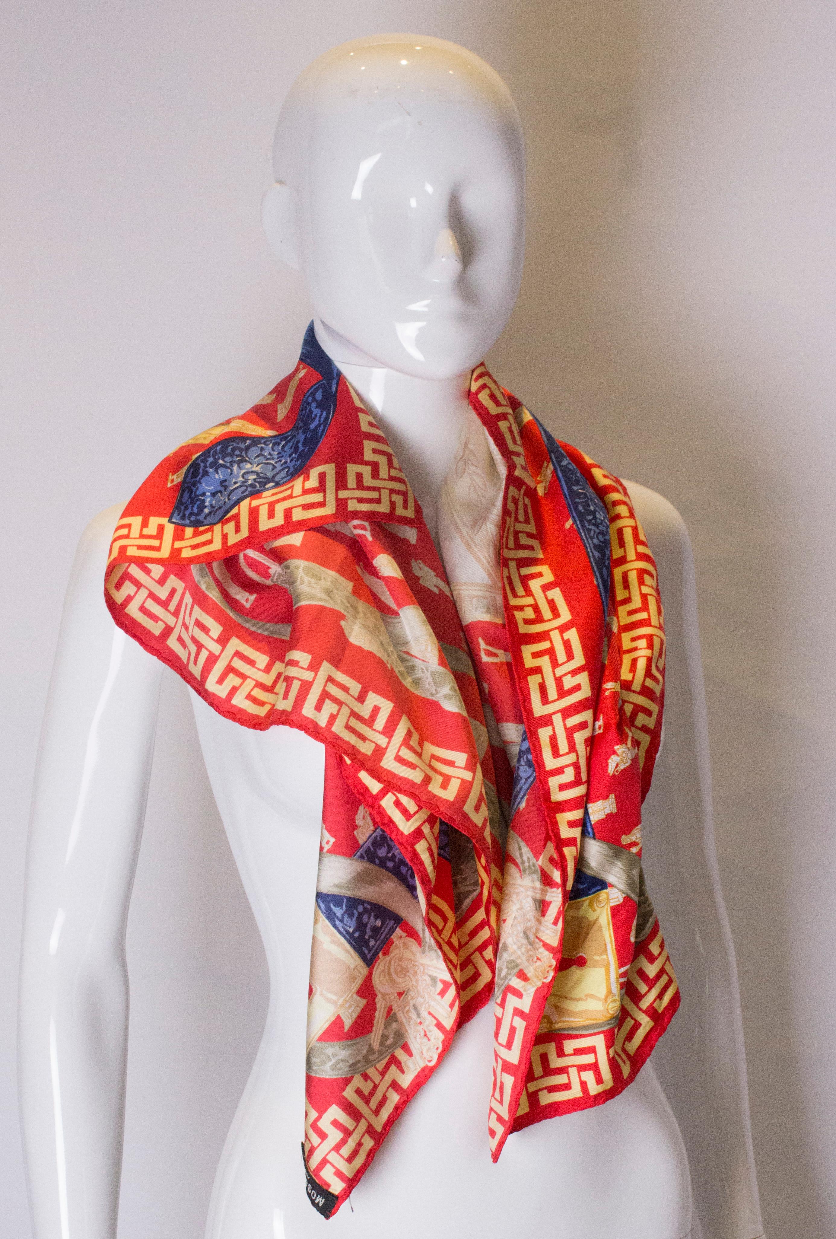 A fun silk scarf by Moschino. The scarf has a red background with gold and blue design.