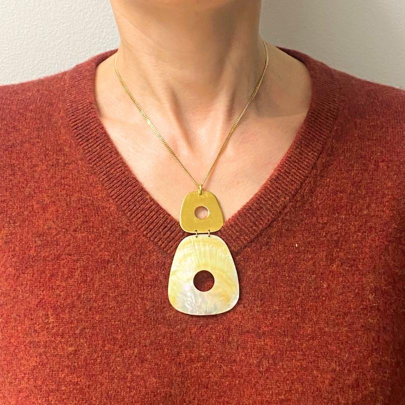 Una collana vintage con ciondolo in madreperla e catena in oro 10k.
Il ciondolo è composto da due pezzi geometrici e lisci: uno superiore di forma quadrata in oro e uno più grande di forma organica in madreperla. Il luccichio naturale del MOP dona