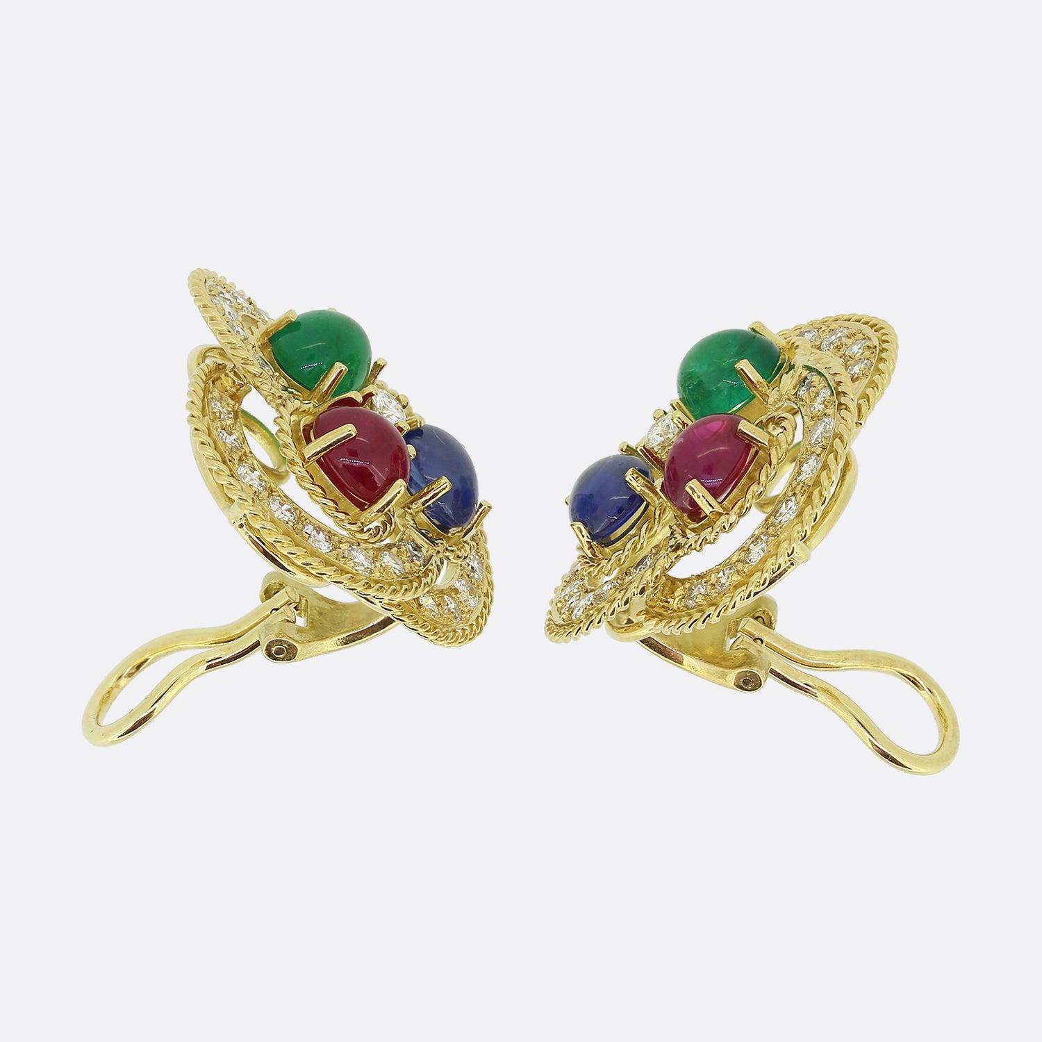 Here we have a delightful pair of vintage cluster earrings. Each piece showcases a trio of oval shaped cabochon gemstones at the centre including a rich red ruby, a bold blue sapphire and vivid green emerald. These focal gemstones are framed by a