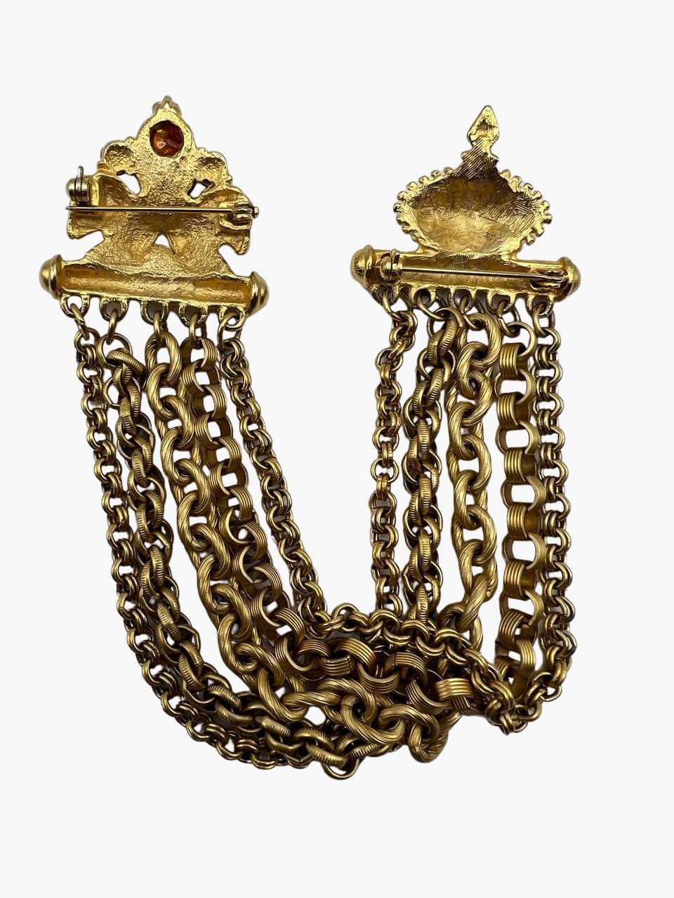Goldfarbene Halskettenbrosche im Vintage-Stil, bestehend aus 5 verschiedenen Ketten, die auf der einen Seite mit einem kronenförmigen Verschluss und auf der anderen Seite mit Widdern verziert sind. 
Größe:  10 cm Länge in geschlossenem Zustand
3,5