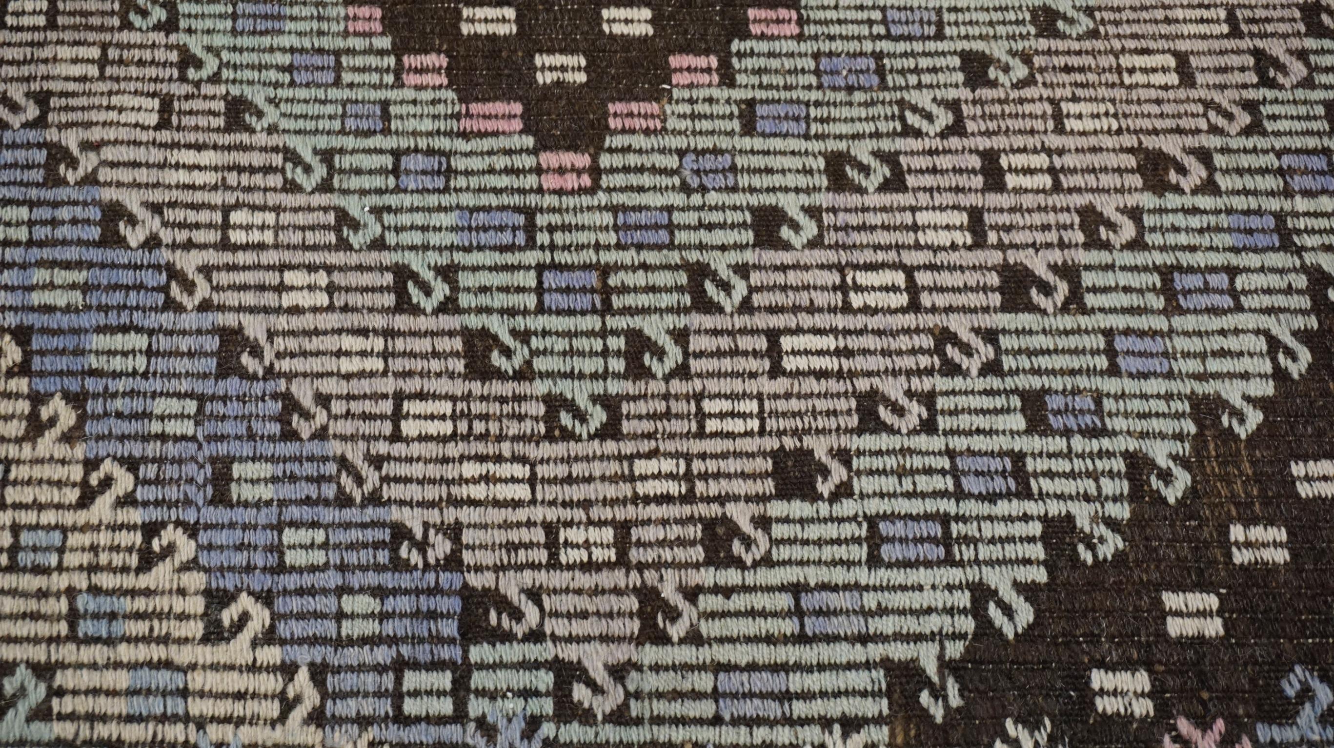 Dieser auffällige Kelimteppich aus Wolle im Vintage-Stil weist ein kühnes geometrisches Rautenmuster auf, das in satten Blau-, Grau-, Lila- und Grüntönen gewebt ist. Das zentrale Feld ist mit einem sich wiederholenden Rautenmotiv verziert, das mit