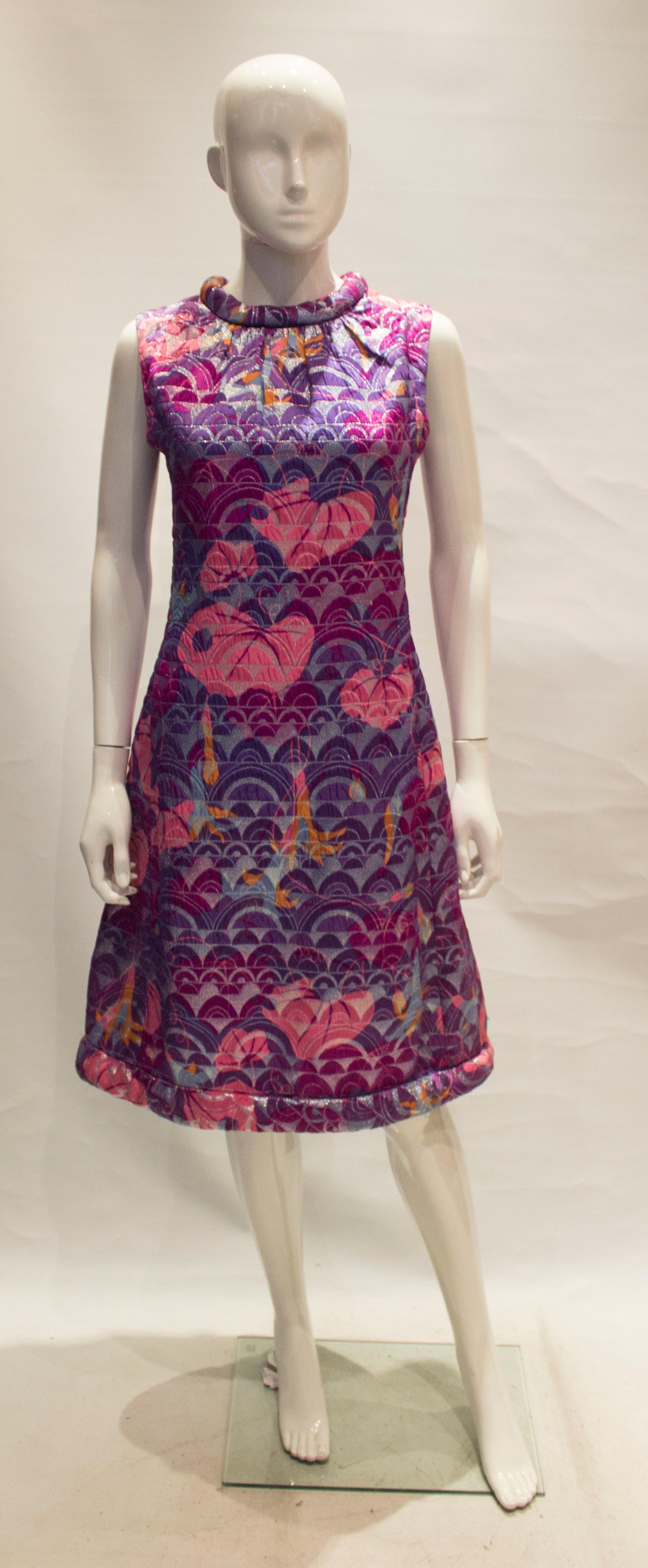 A stunning cocktail dress in shades of purple and pink, and with an unusual padded hem and neckline. The dress has a bow detail at the back and a central back zip and is fully lined.
