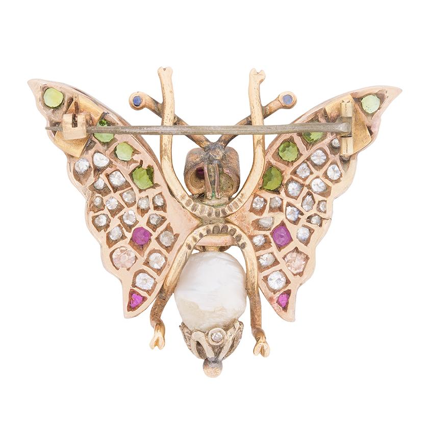 Diese Vintage-Schmetterlingsbrosche aus den 1930er Jahren ist mit einer skurrilen Kombination aus Diamanten, grünen Granaten, rosa Saphiren, blauen Saphiren und einer Perle besetzt.

Ihre farbenfrohen Flügel glänzen mit einer Reihe von Steinen im