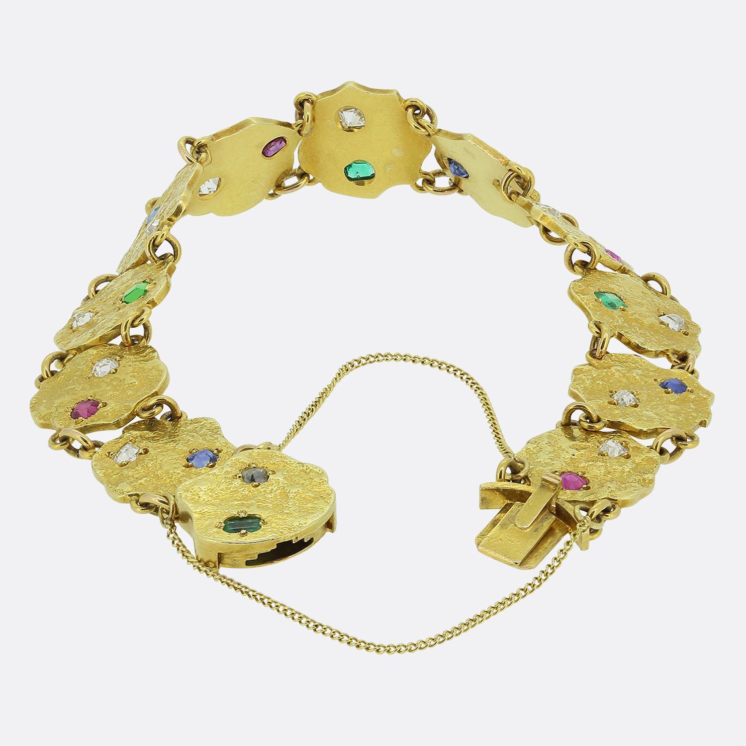 Aquí tenemos una pulsera maravillosamente única fabricada en oro amarillo de 18 quilates. Esta pieza presenta una serie de eslabones planos martillados, cada uno de ellos conectado mediante una cadena corta y adornado con un par de vibrantes piedras