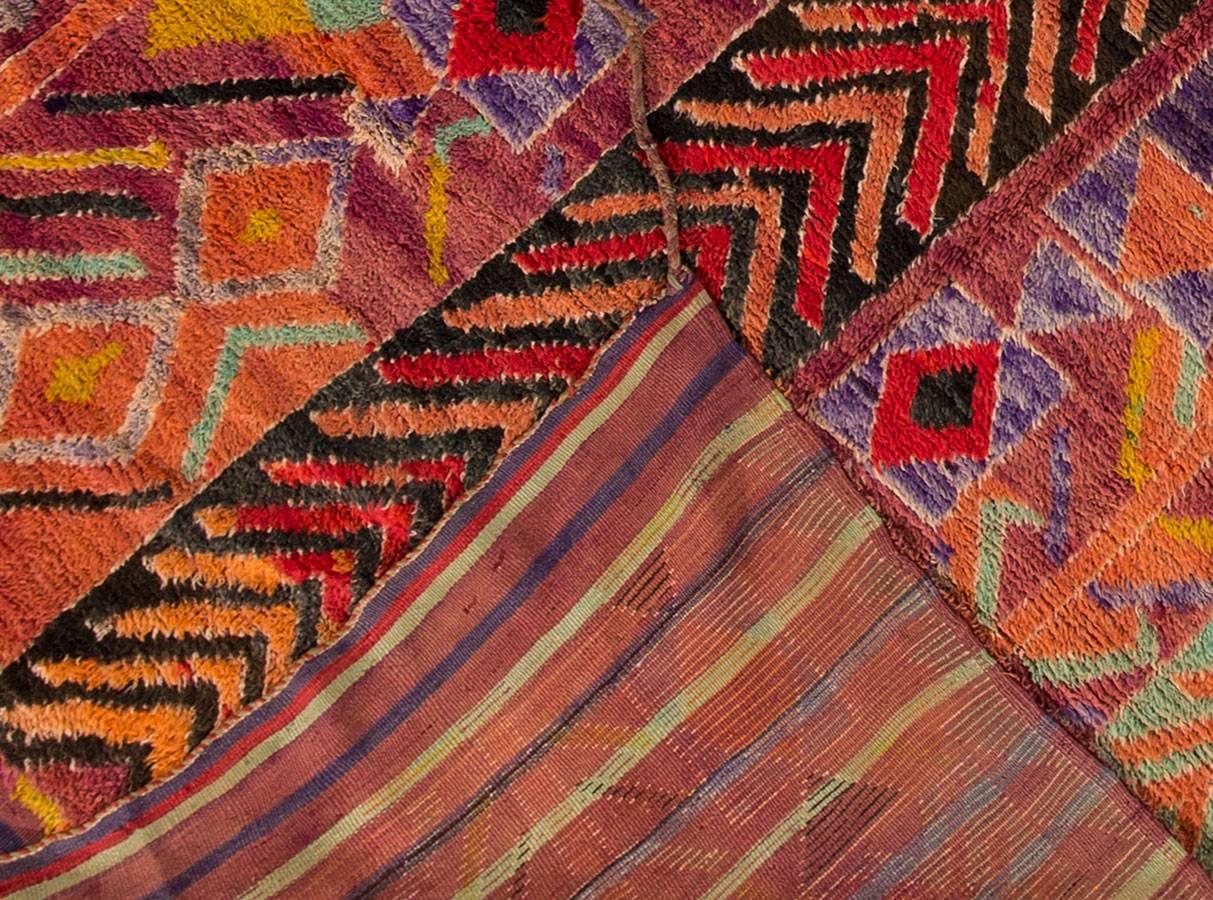 Vintage 1960s Moroccan carpet. This piece has an eggplant-purple field with a multicolored, geometric design in vertical stripes. Each stripe has a differently colored, chevron style or general geometric design as well. Measures: 6 x 13.10.