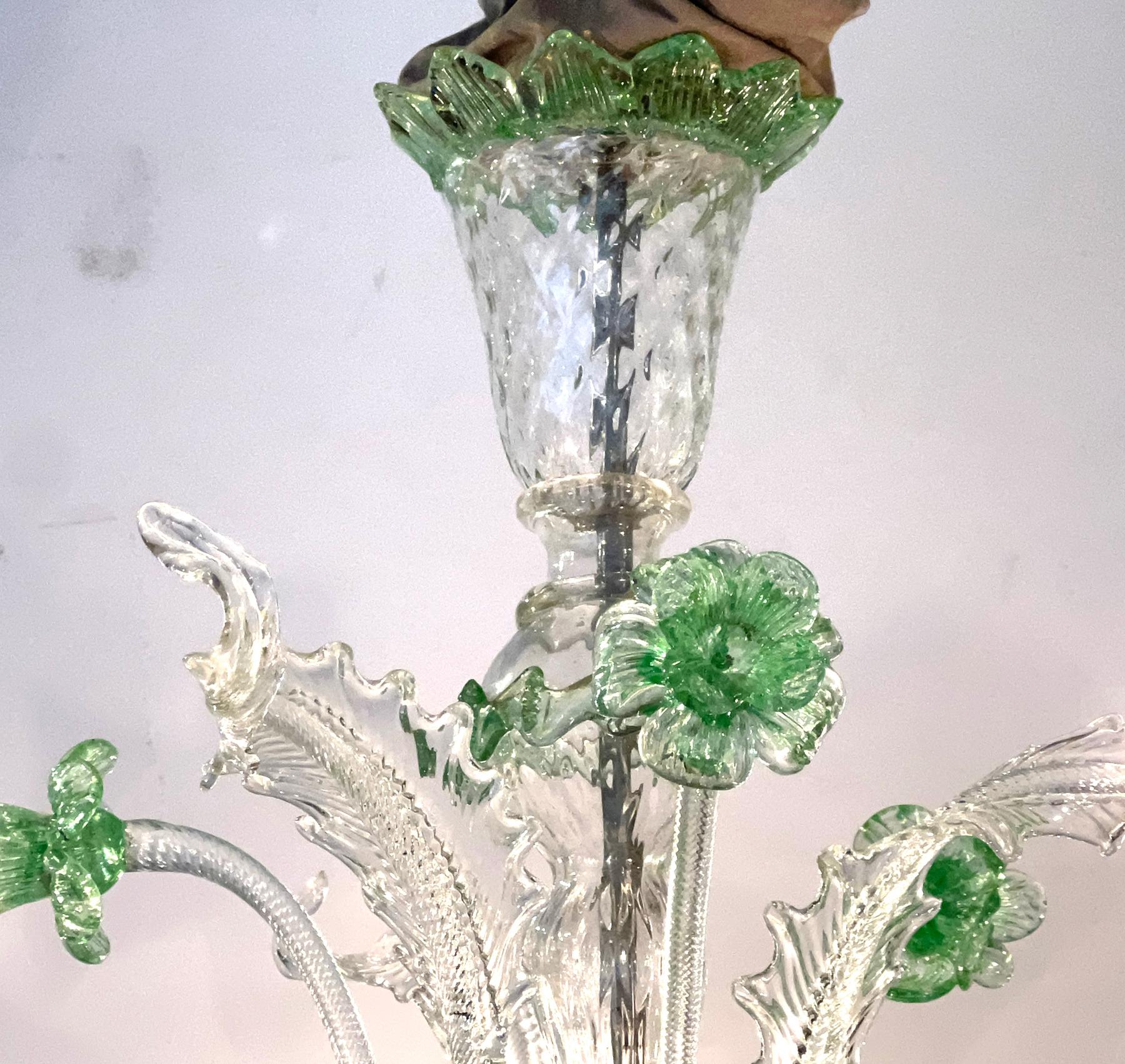 lampadario in vetro di Murano dal design classico, con supporto centrale a forma di balsuster rovesciato e baldacchino svasato, che sovrasta una coppa di vetro con cinque alti steli a rosetta e fogliame, intervallati da cinque foglie basse e