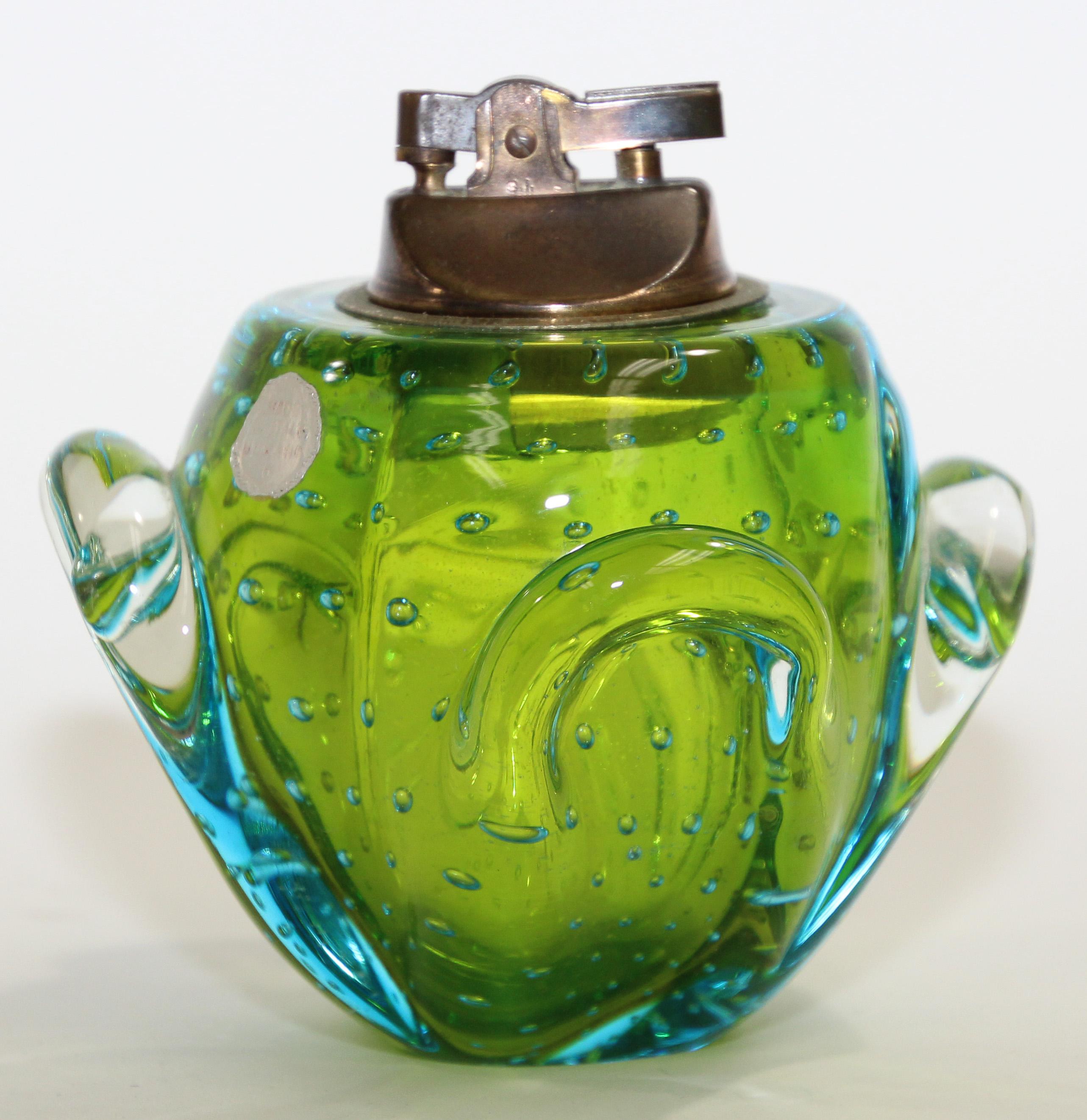 Vintage retro 1970s heavy Murano green and blue glass table lighter-paperweight with brass.
A dramatic accent to any modern living room decor, this Murano lighter will elevate any coffee table or desk surface with its timeless allure.
Measures: