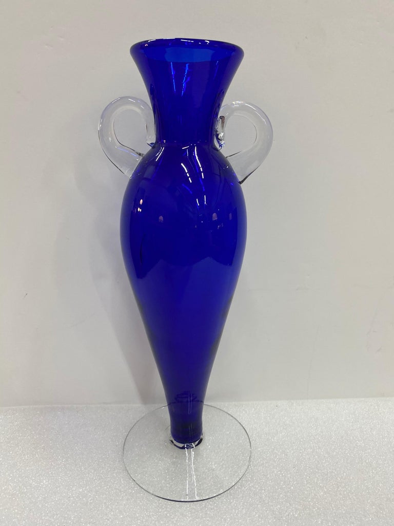Vintage Italian Murano cobalt blue mouth blown art glass vase. This beautiful vase has small clear glass handles yielding a lovely stature. When the light hits the glass the blue glass glows. The vase will make an impressive addition to any decor.