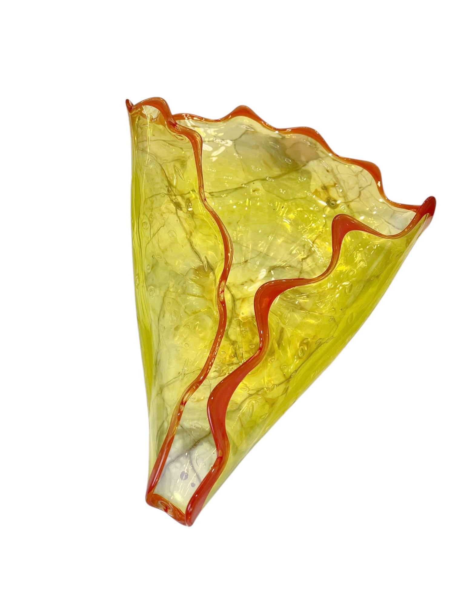 Un vivace piatto d'epoca in vetro di Murano, soffiato a mano in un sorprendente giallo con un audace bordo arancione. La forma fluida e piegata cattura la maestria e il movimento che caratterizzano la lavorazione del vetro di Murano, mentre i colori