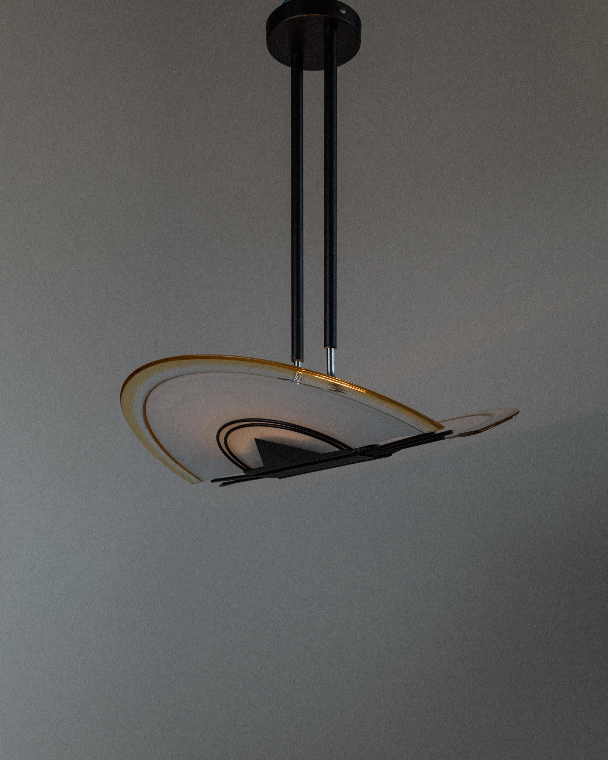 Esta lámpara de techo vintage de cristal de Murano de los años 80 captura la atrevida estética de la época de Memphis con una forma única inspirada en el Art Decó. El marco de metal negro presenta tres puntales geométricos que sujetan dos grandes