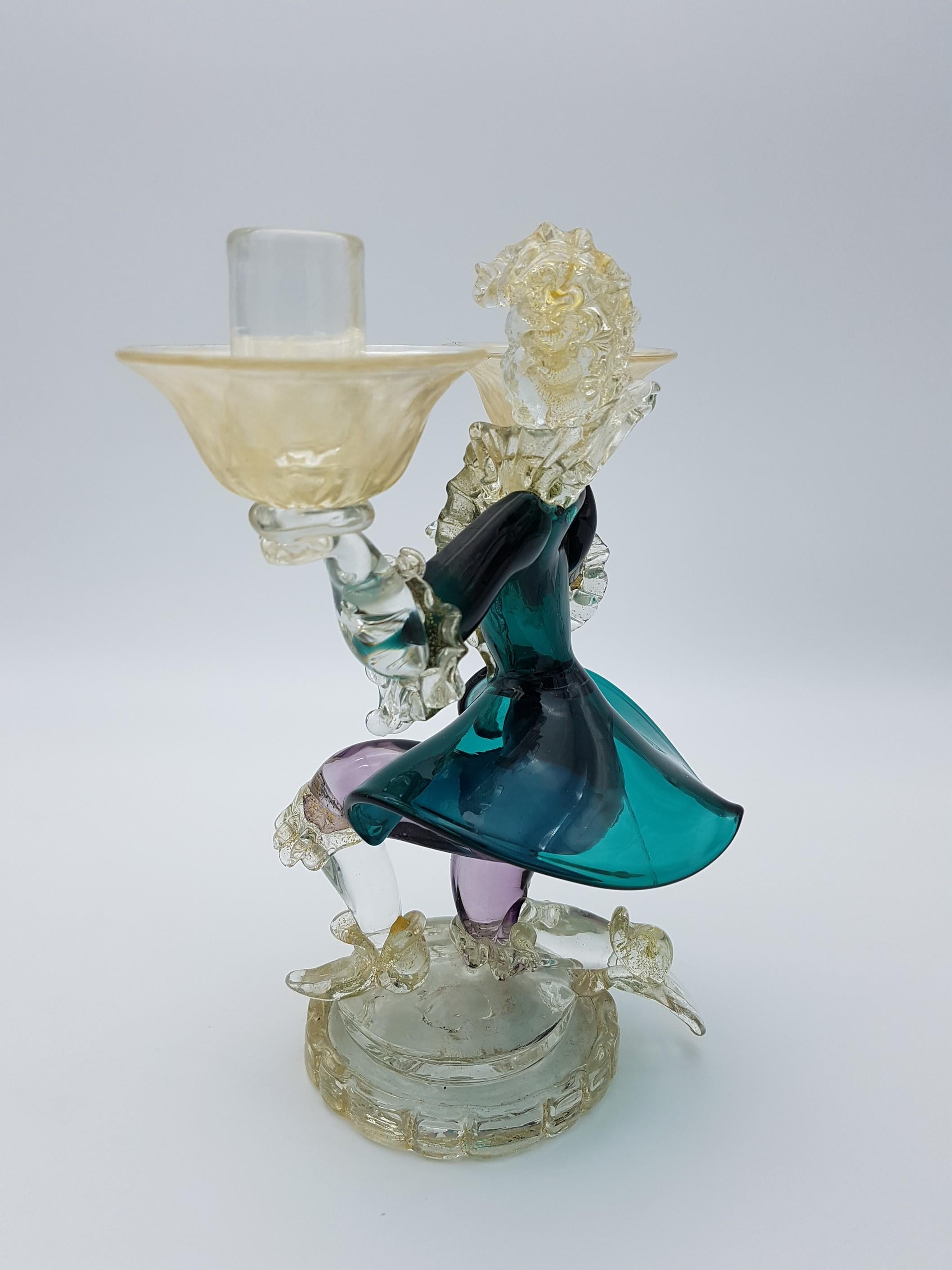 This vintage Murano glass figurine was hand-made by Gino Cenedese e Figlio in the early 1970s and portrays a Venetian nobleman from the 1700s, knealed and carrying on his hands two candleholders. While the 1700s represented a period of decadence and