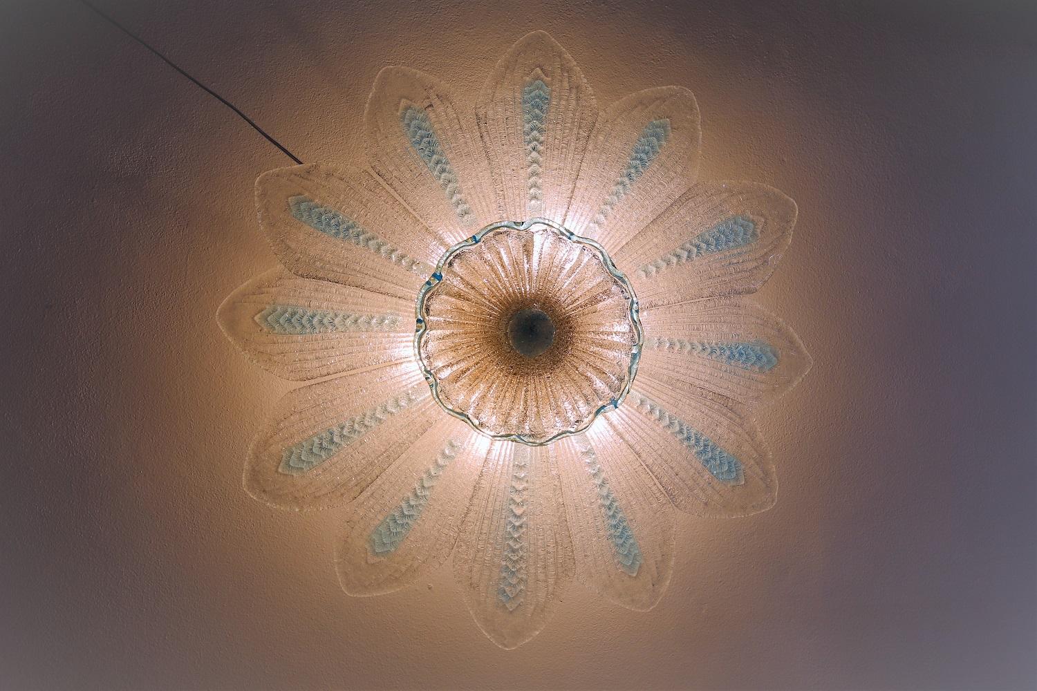 Large ceiling lamp in the shape of a big flower consisting of 12 large glass petals, a central glass rosette and closing glass button.
Made in Italy in the style of Barovier & Toso, Murano, in the 1970s.
The thick transparent glass with light blue