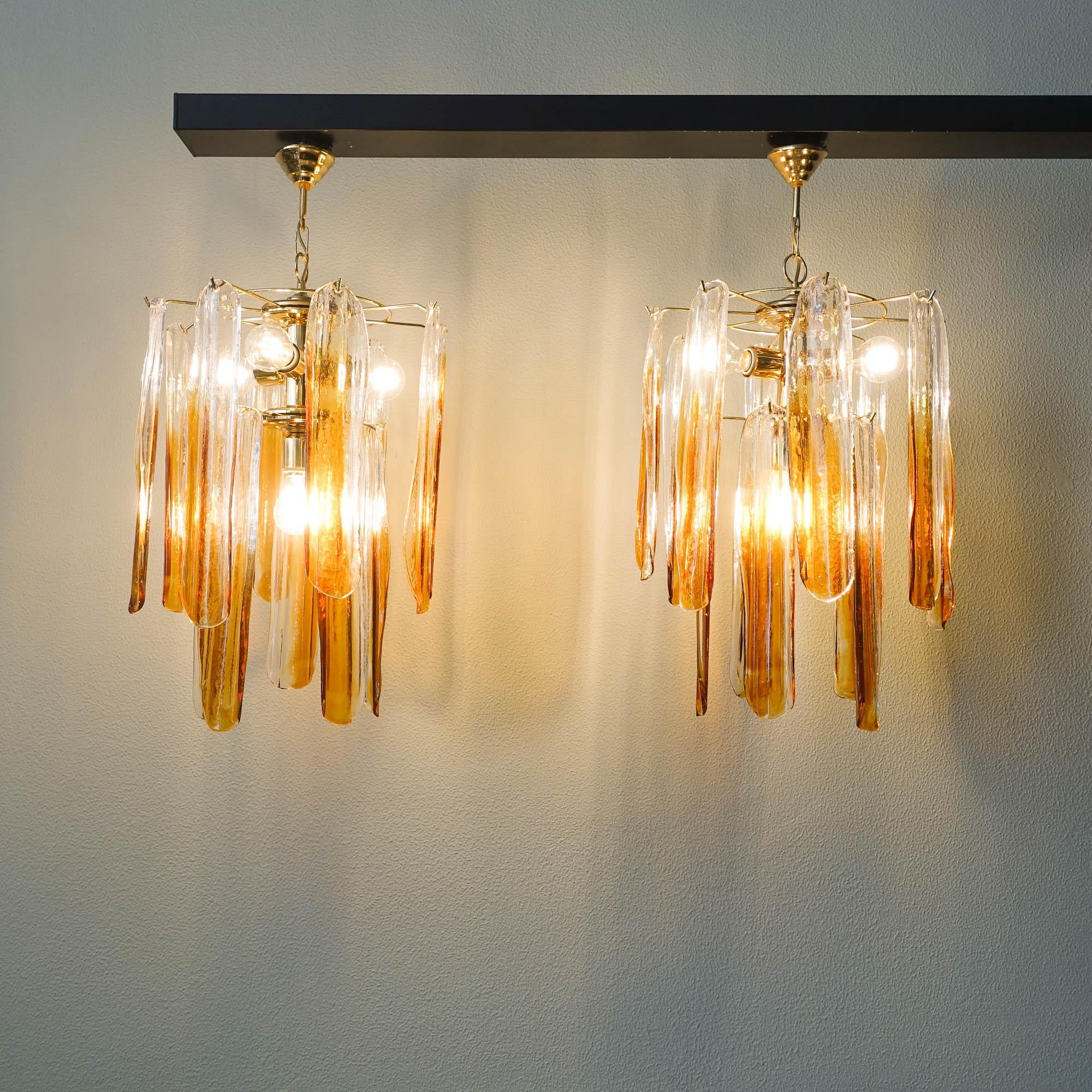 This pair of Murano glass chandeliers was designed by Carlo Nason and produced by Mazzega, in Italy, during the 1970's. Each lamp features twelve organic-shaped Murano glass plates, running from clear to amber that nicely diffuse the light.  Each