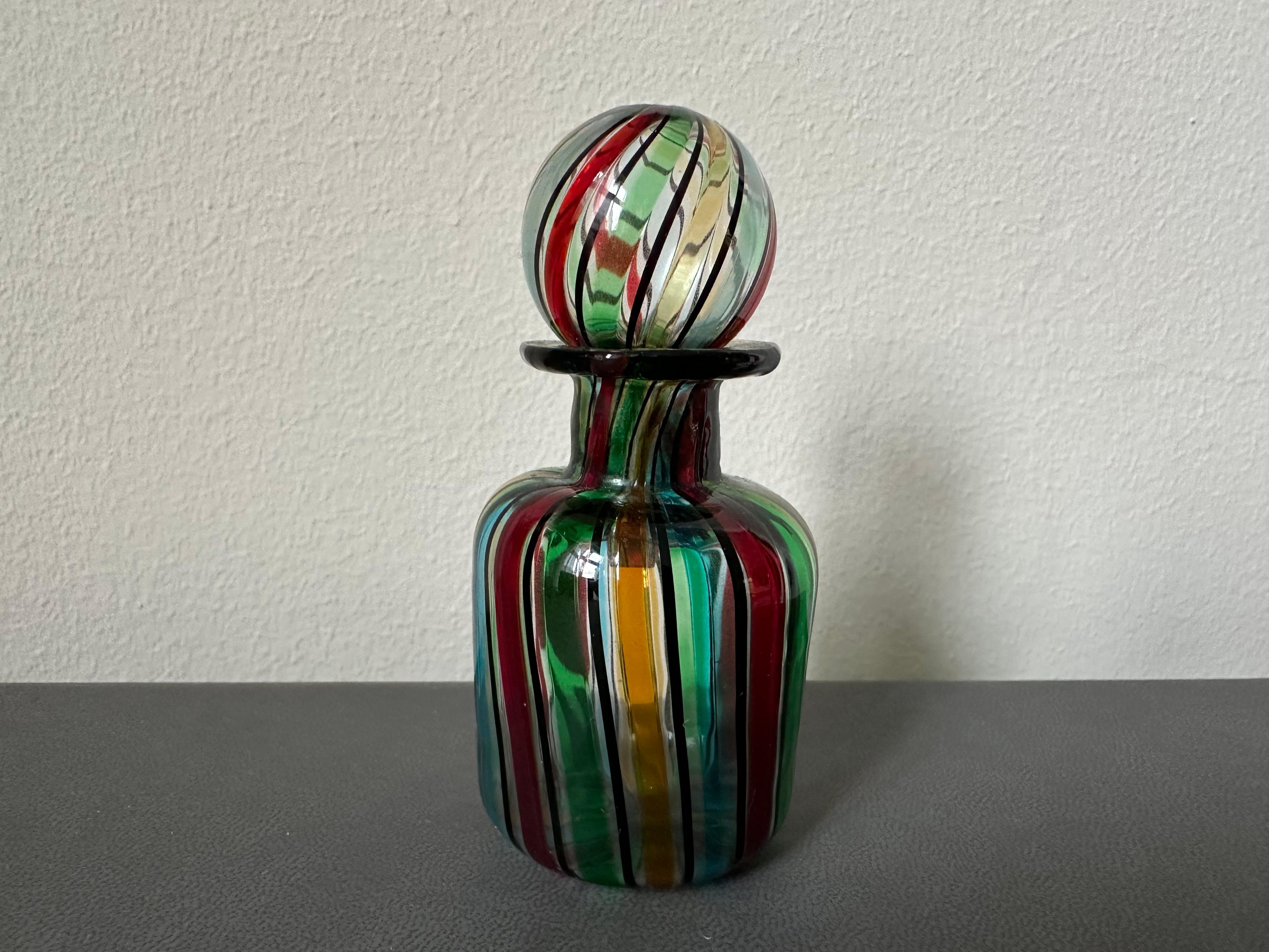 This delicate vintage perfume bottle, crafted from exquisite Murano glass in the 1950s, is a true testament to Italian artistry. Featuring colorful band inclusions in vibrant stripes, the design showcases the timeless craftsmanship for which Murano