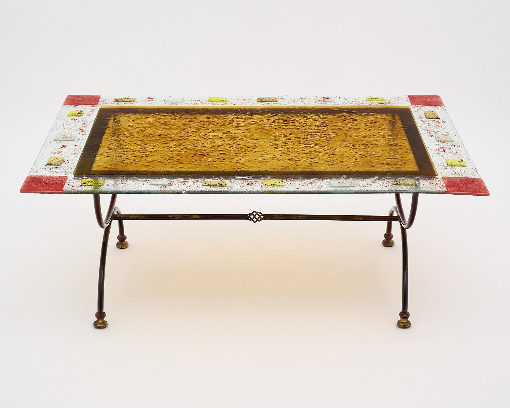 Coffee table, Italian, from the Veneto region. This piece has a hand-hammered forged iron base supporting a slab of Murano glass featuring a colorful fused glass decor.
