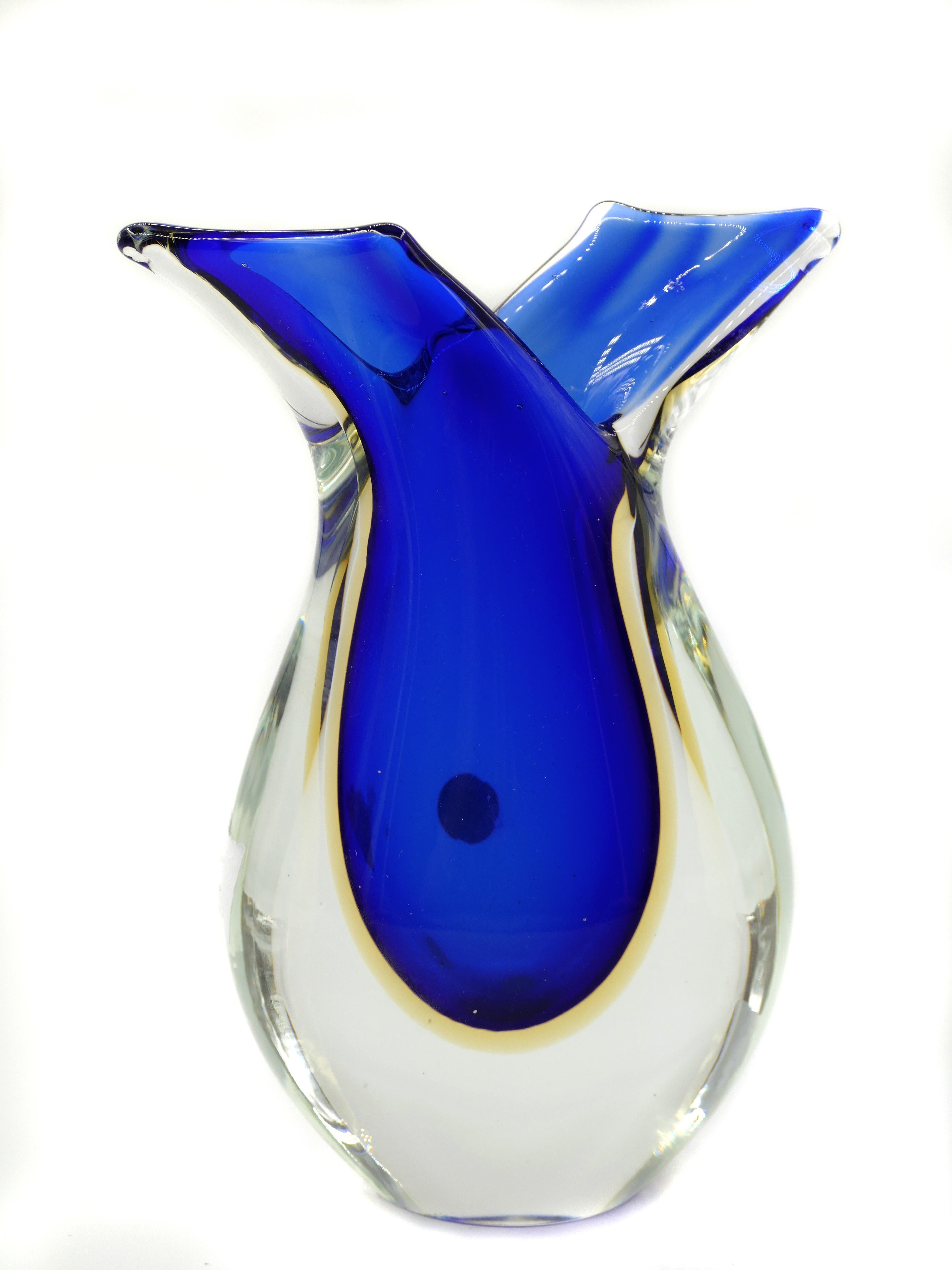 Questo vaso in vetro di Murano blu è un bellissimo vaso made in Italy prodotto alla fine del XX secolo. 

Con un gioco di contrasti tra il vetro trasparente e quello blu, il design sinuoso e in ottime condizioni, questo pezzo è assolutamente da