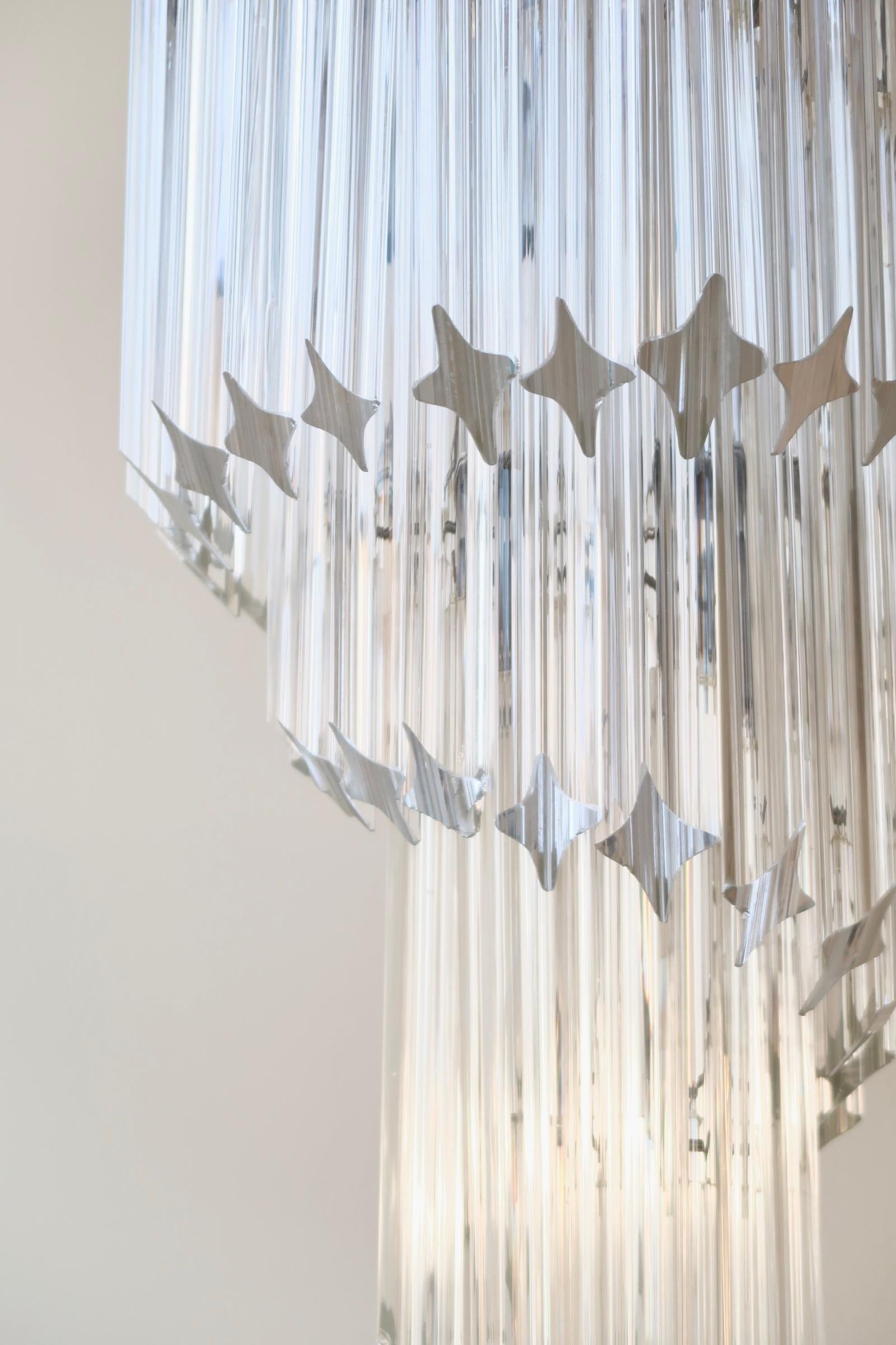 The chandelier consists of 54 mouth-blown quadridri prisms / glass rods in a transparent glass set on a chrome frame. It has 5 x E14 sockets (max. 60W) and provides plenty of light. Handmade in Italy. A certain proportion of the prisms have typical