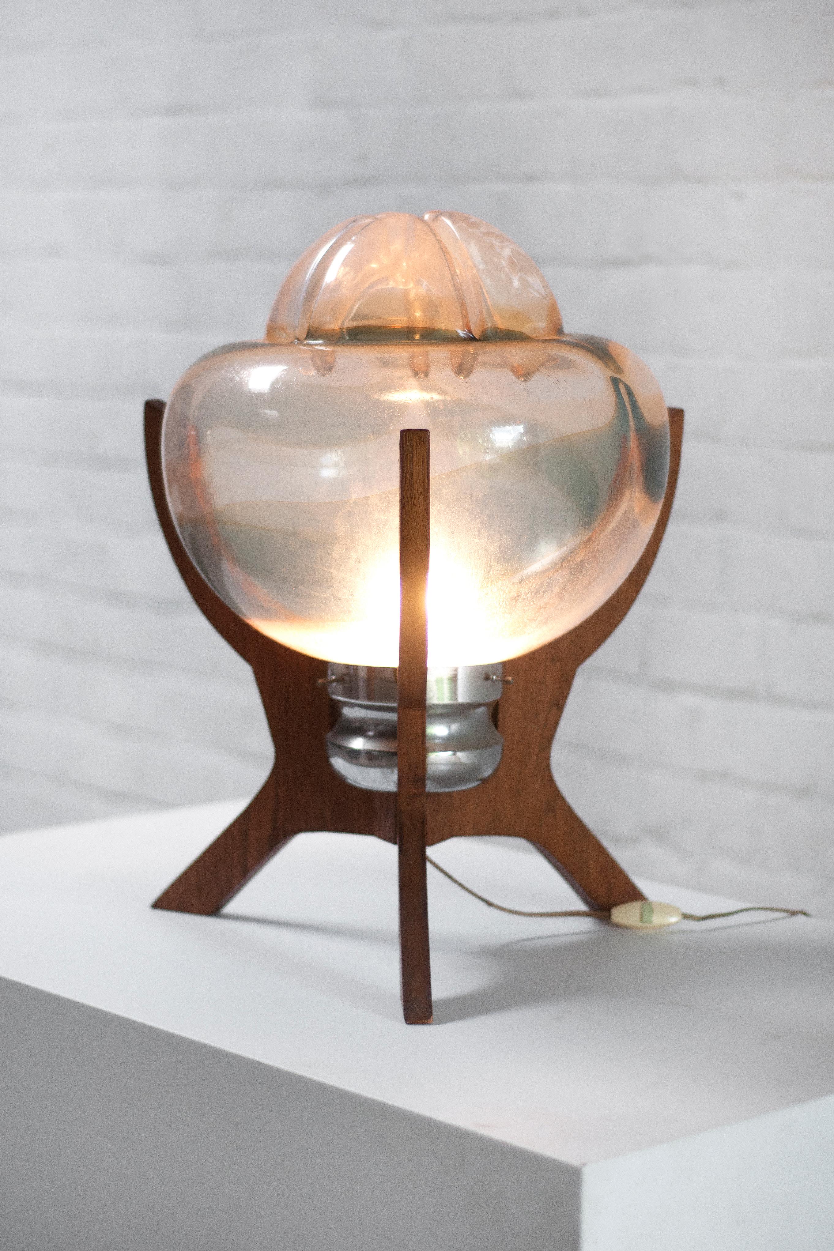 A very peculiar and never before seen table lamp made out of a large murano glass shade with a sculptural wooden base. Possibly italian but the origin is unsure. A very decorative piece that would without a doubt be the centre of attention in any