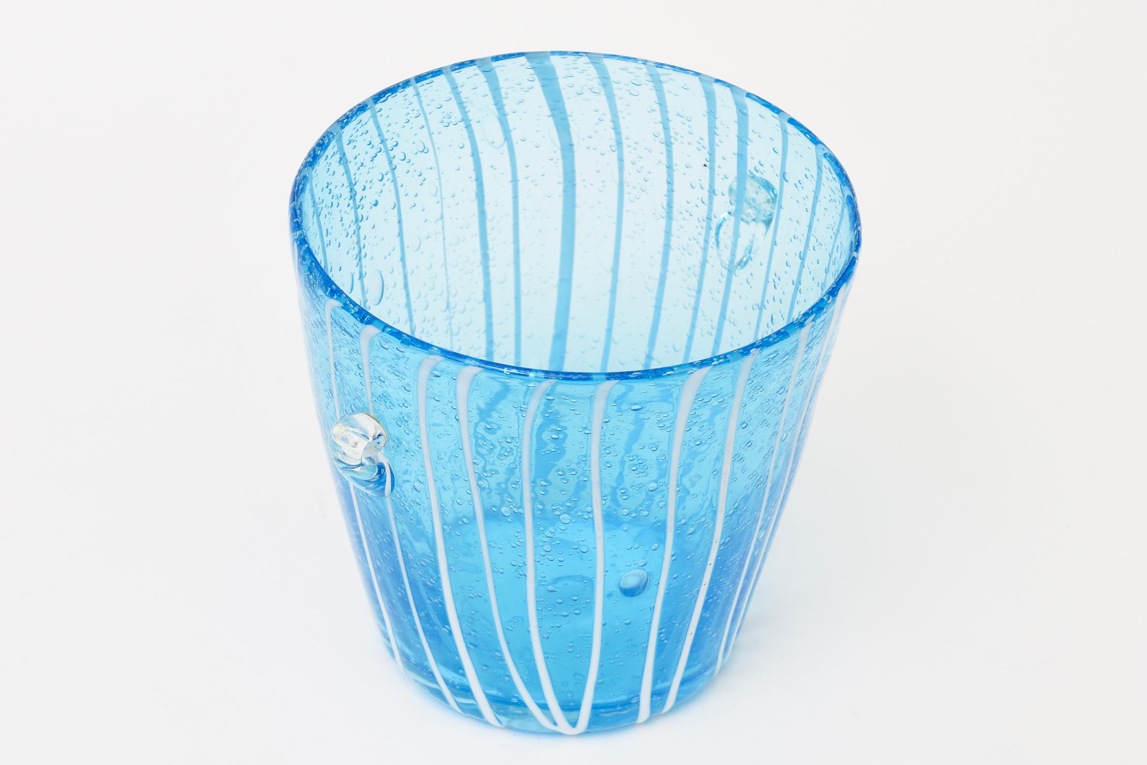 Thiscompact Murano vintage ice bucket was commssioned by the Italian Liquor Company called Disaranno to Venini.
It is sapphire blue turquoise with white lines. It has small clear appendage handles on the side. Great barware with beautiful color.