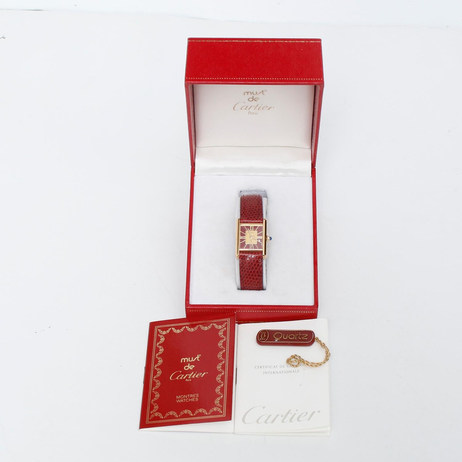 Montre Vintage Must de Cartier Vermeil Or Bourgogne pour femme - Mouvement à quartz. Argent sterling plaqué or jaune 18k (22mm x 28mm). Cadran rouge avec index en or. Bracelet bourgogne avec boucle en or plaqué. D'occasion avec la boîte et le livre