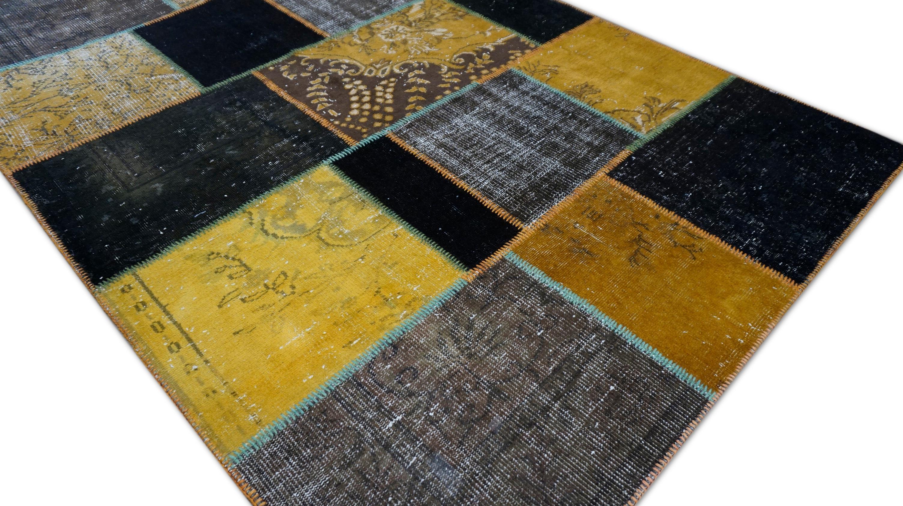 Questo caratteristico tappeto patchwork in lana, tessuto a mano, presenta una composizione sapientemente curata di frammenti di tappeti vintage sovratinti in una ricca tavolozza di tonalità senape, nero carbone e marrone terra. Meticolosamente