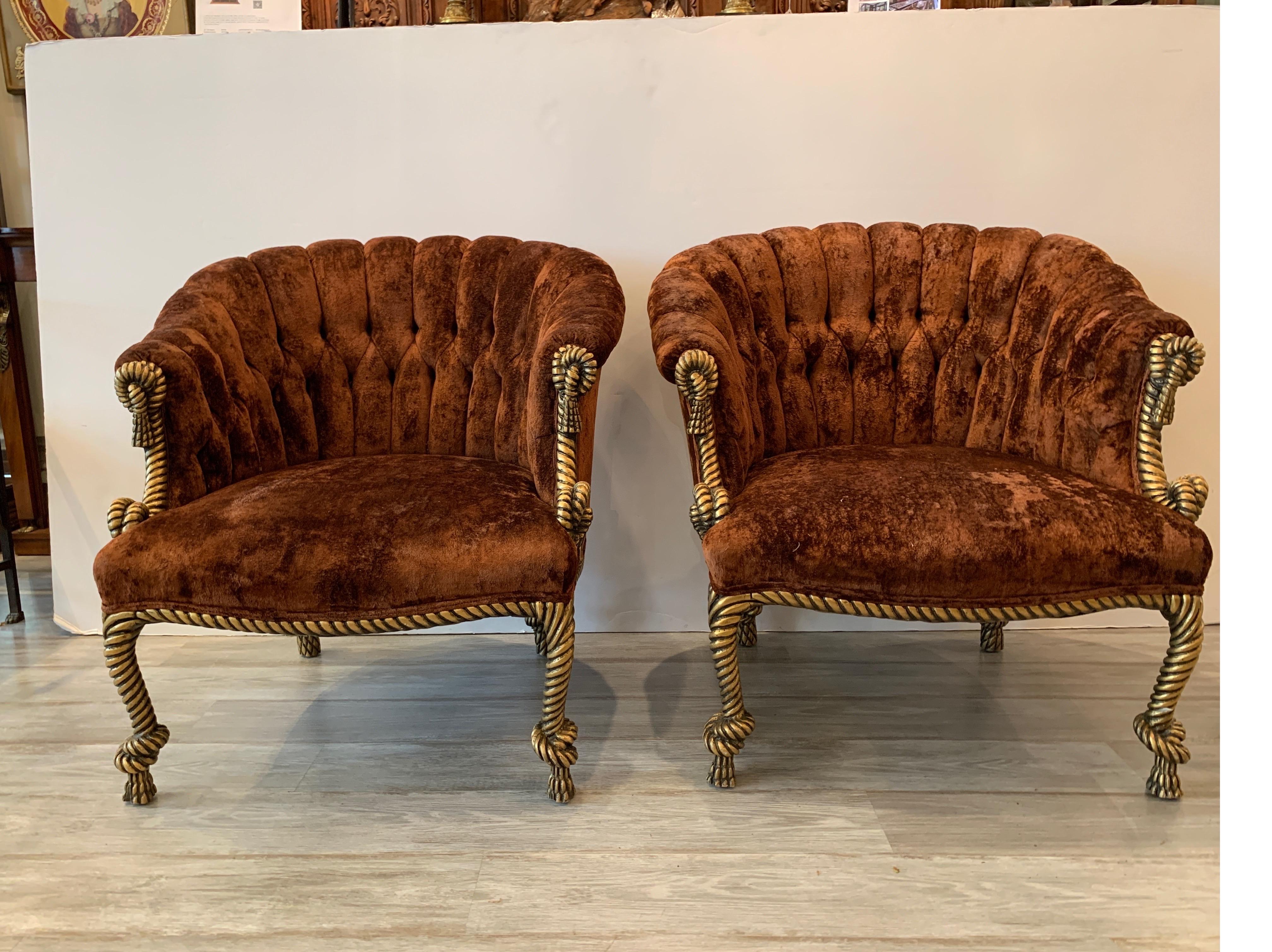 Lovely pair of 1960s Hollywood Regency barrel back armchairs with carved wood rope and tassel motif. The gilt frames with original iron rust red velvet covering. The fabric in good shape but would recommend reupholstering.