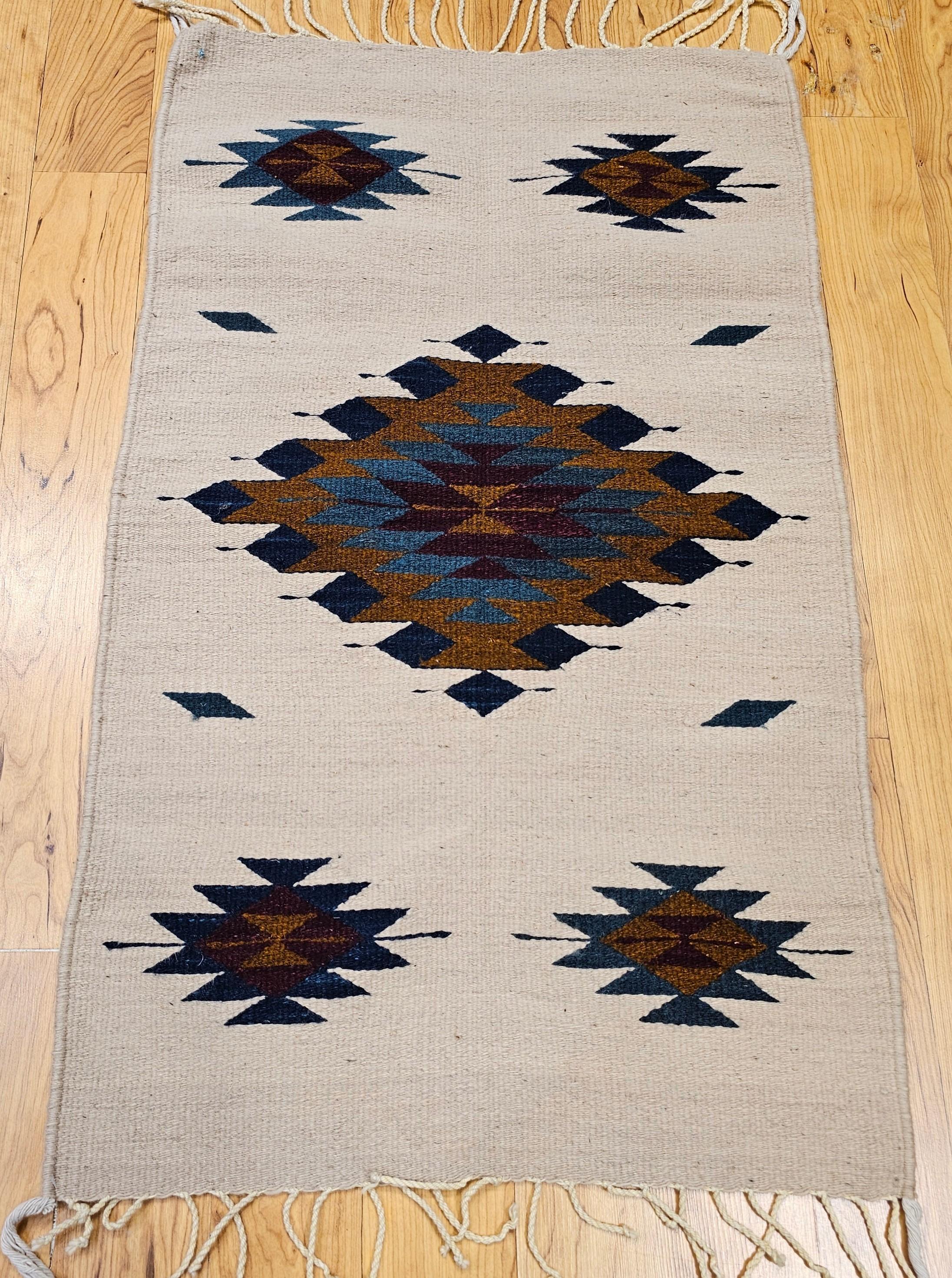 This vintage Native American Navajo area rug, crafted circa the mid-1900s, features a striking single diamond central medallion design, a classic motif in Navajo weaving. Woven in a rich, earthy palette of ivory, blue, burgundy, and brown, this rug