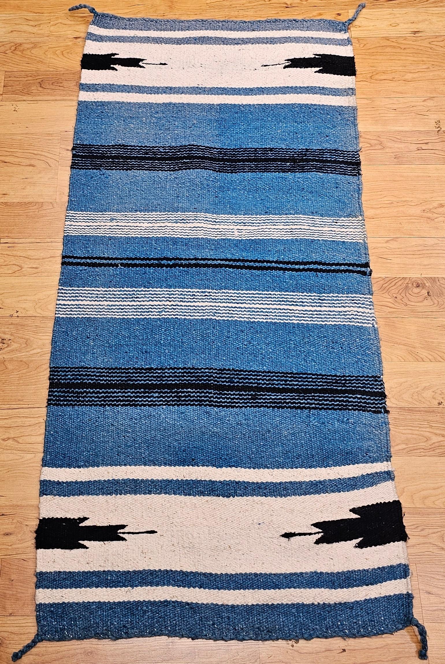 Alfombra vintage Navajo de color azul persa, con acentos de color marfil y negro.  La alfombra navajo vintage tiene un patrón de rayas de fondo en un tono azul muy singular y hermoso, acentuado con tiras estrechas en marfil y reverso.   Las