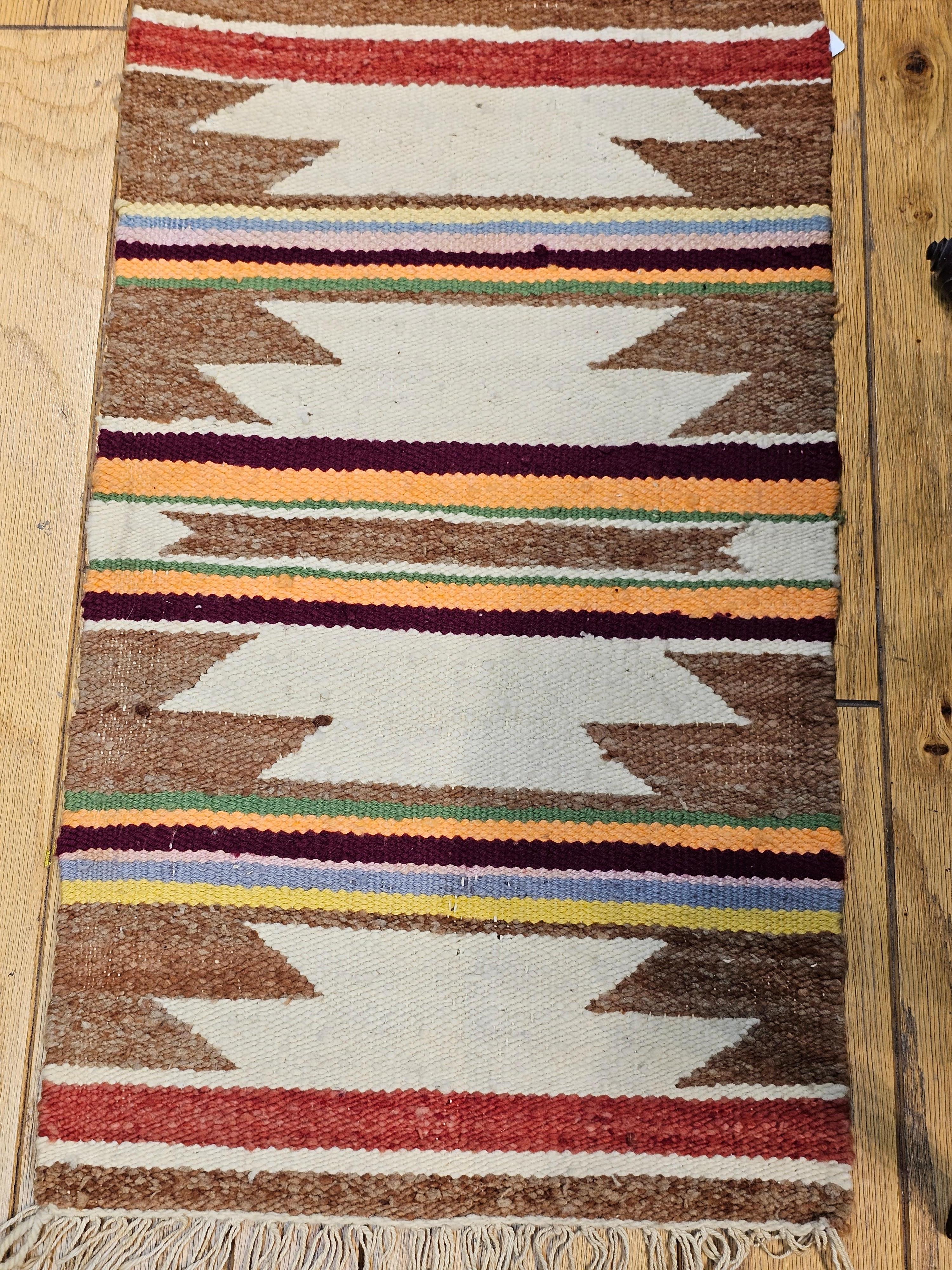 Vintage native American Navajo area rug in a wide band pattern in ivory, rust, purple, and yellow colors from the late 2oth century.  Navajo rugs are generally flat woven with wool for the body of the rug and usually cotton foundation. 
Navajo rugs