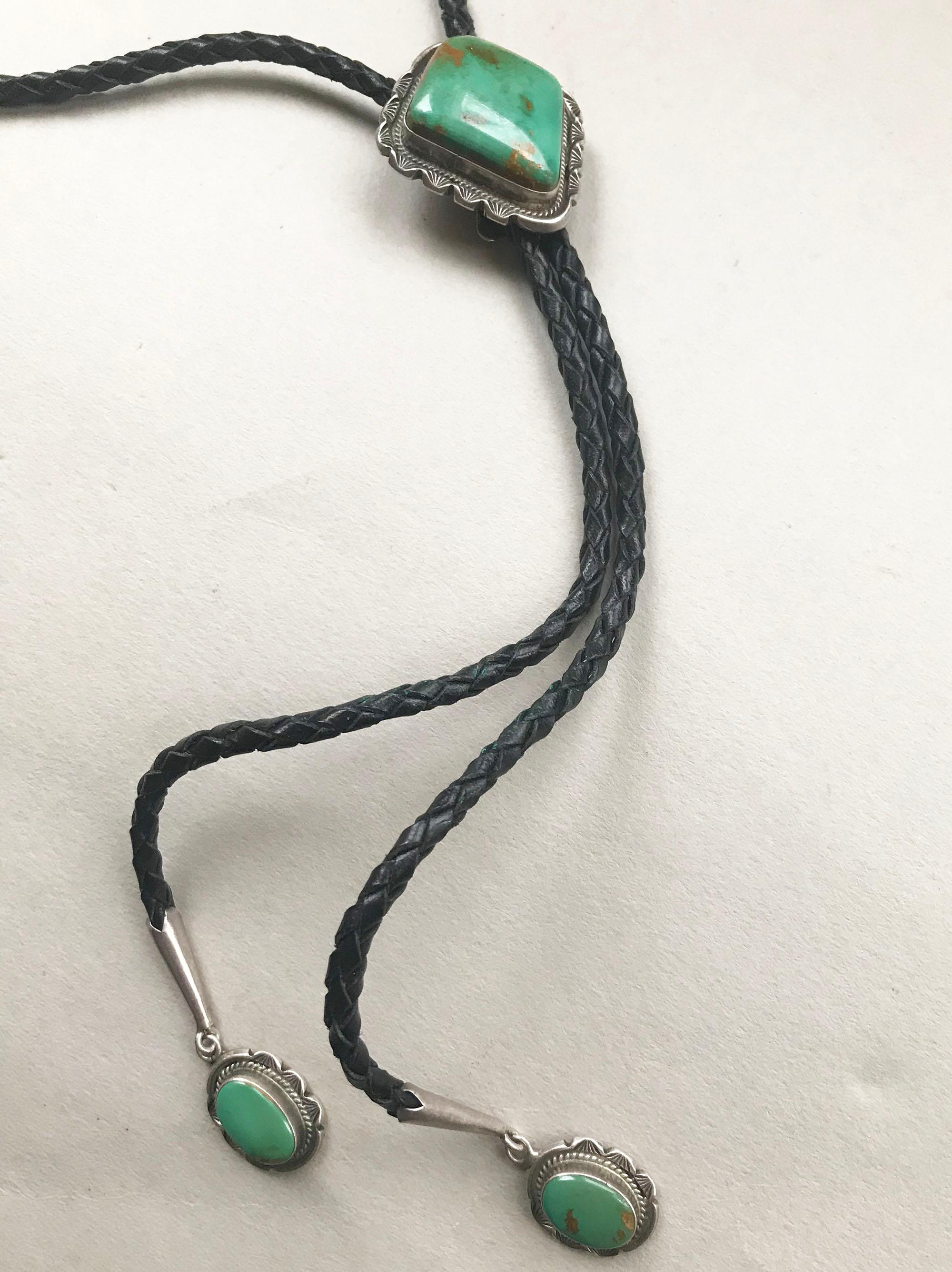 A handsome hand-crafted Navajo design Bolo tie in sterling silver with blue green turquoise 
circa 1960s.
With plaited black leather tie and sterling & turquoise tips.
Measures: 2 x 1 3/4