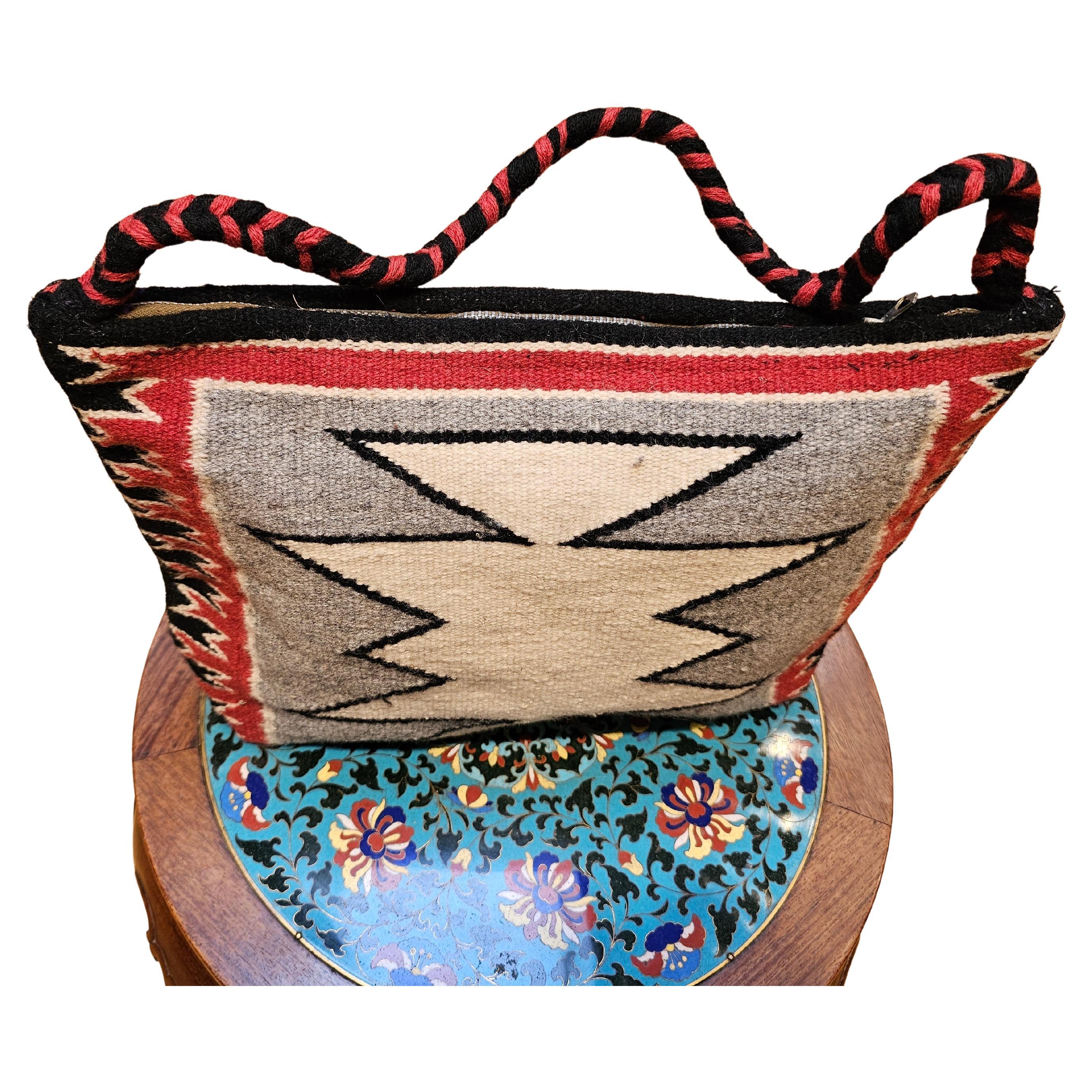 Esta exclusiva bolsa vintage de alfombra navajo, fabricada hacia mediados del siglo XIX, es una hermosa pieza reutilizada a partir de una alfombra navajo original. Con un clásico diseño de rombos en marfil, rojo, gris y negro, este bolso único en su