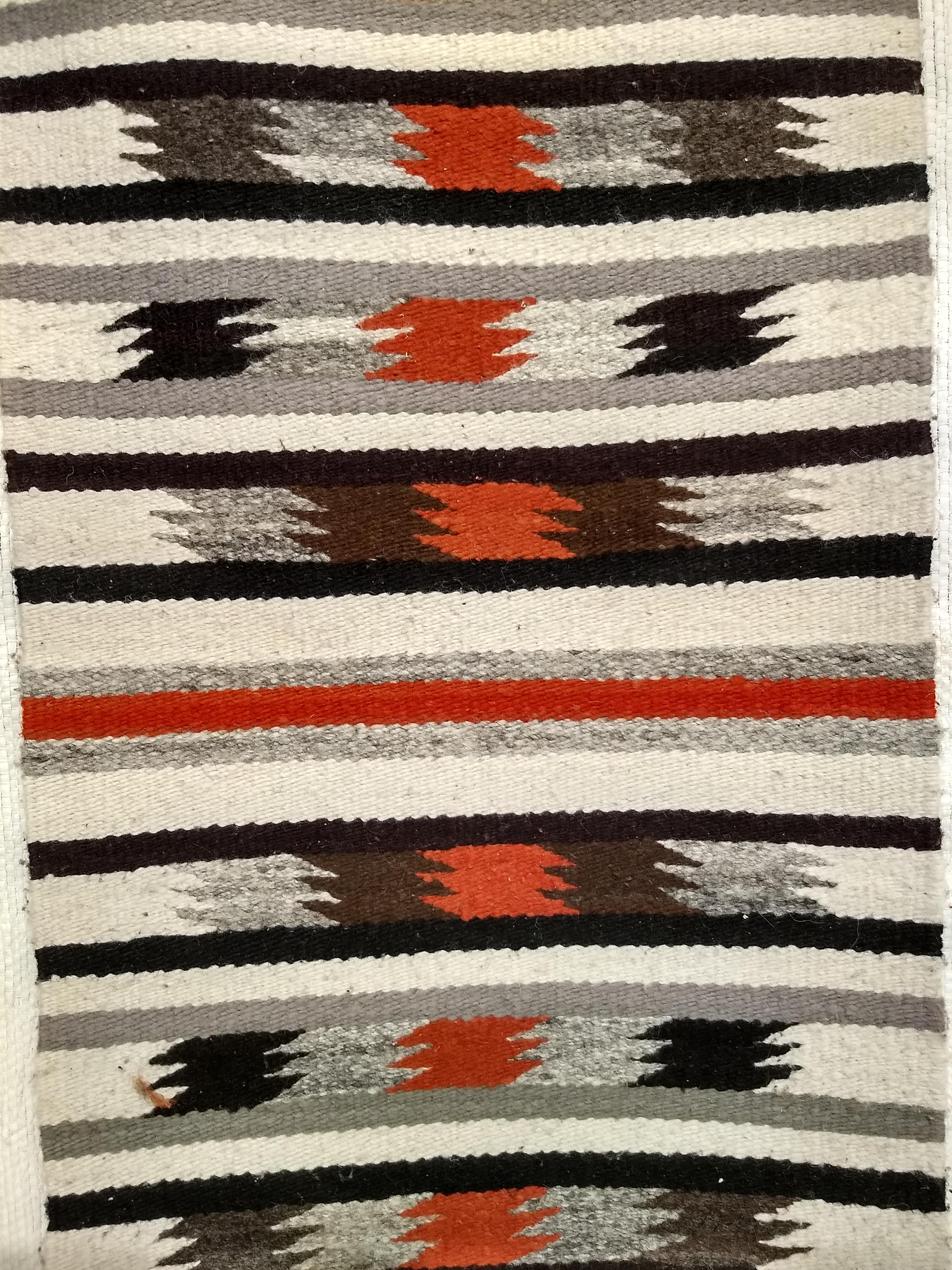 Wonderful vintage Native American Navajo rug in a stripe pattern with southwestern desert colors including gray, black, ivory, and rust-red.  It is perfect as wall art or display on a table. 
Navajo rugs are generally flat woven with wool for the
