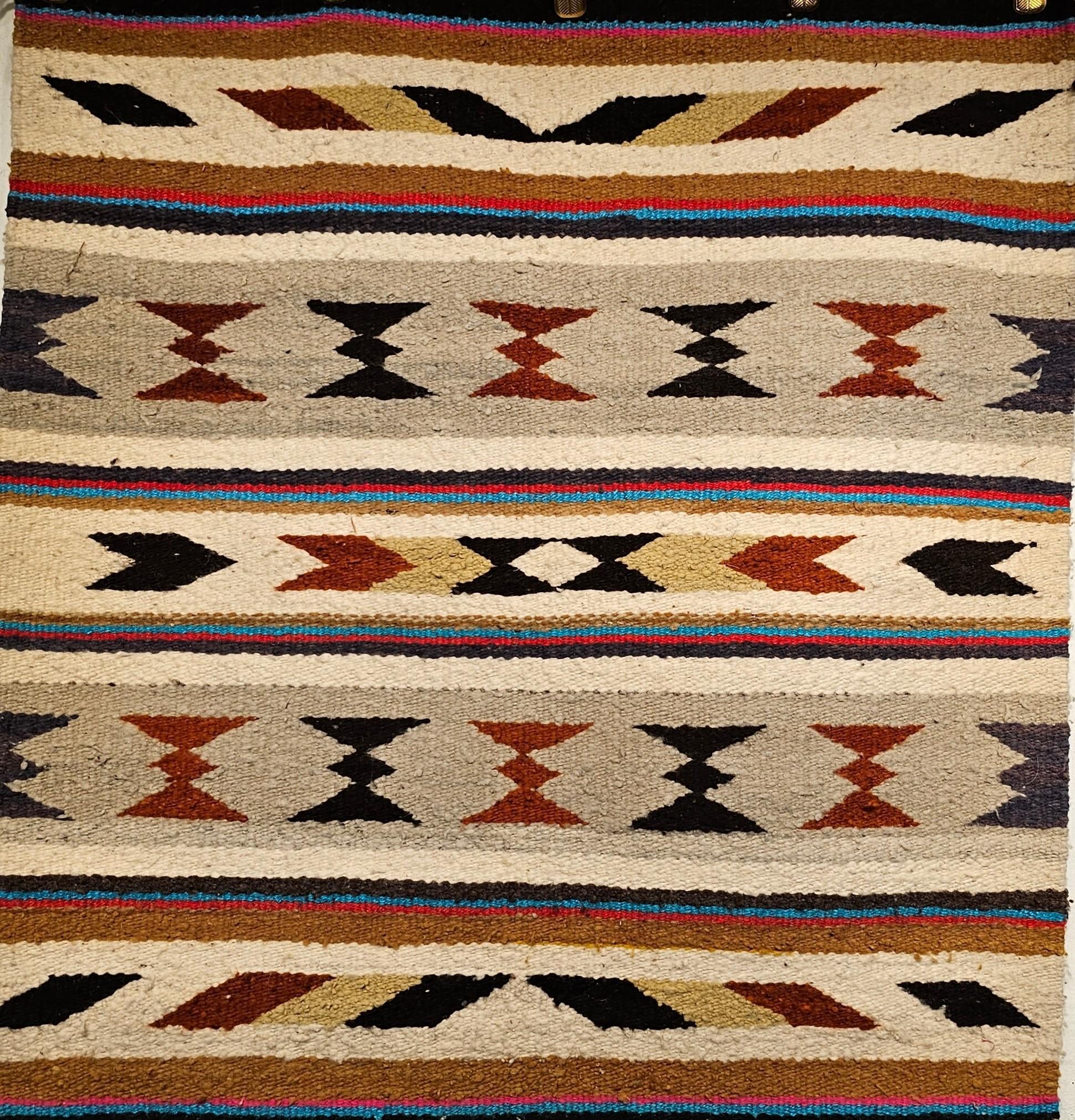 Vintage Native American Navajo saddle blanket in striped pattern from the 3rd quarter of the 1900s.  There is a series of geometric designs in bands that alternate between bands.  The colors in this Navajo rug are in beautiful earth tones including