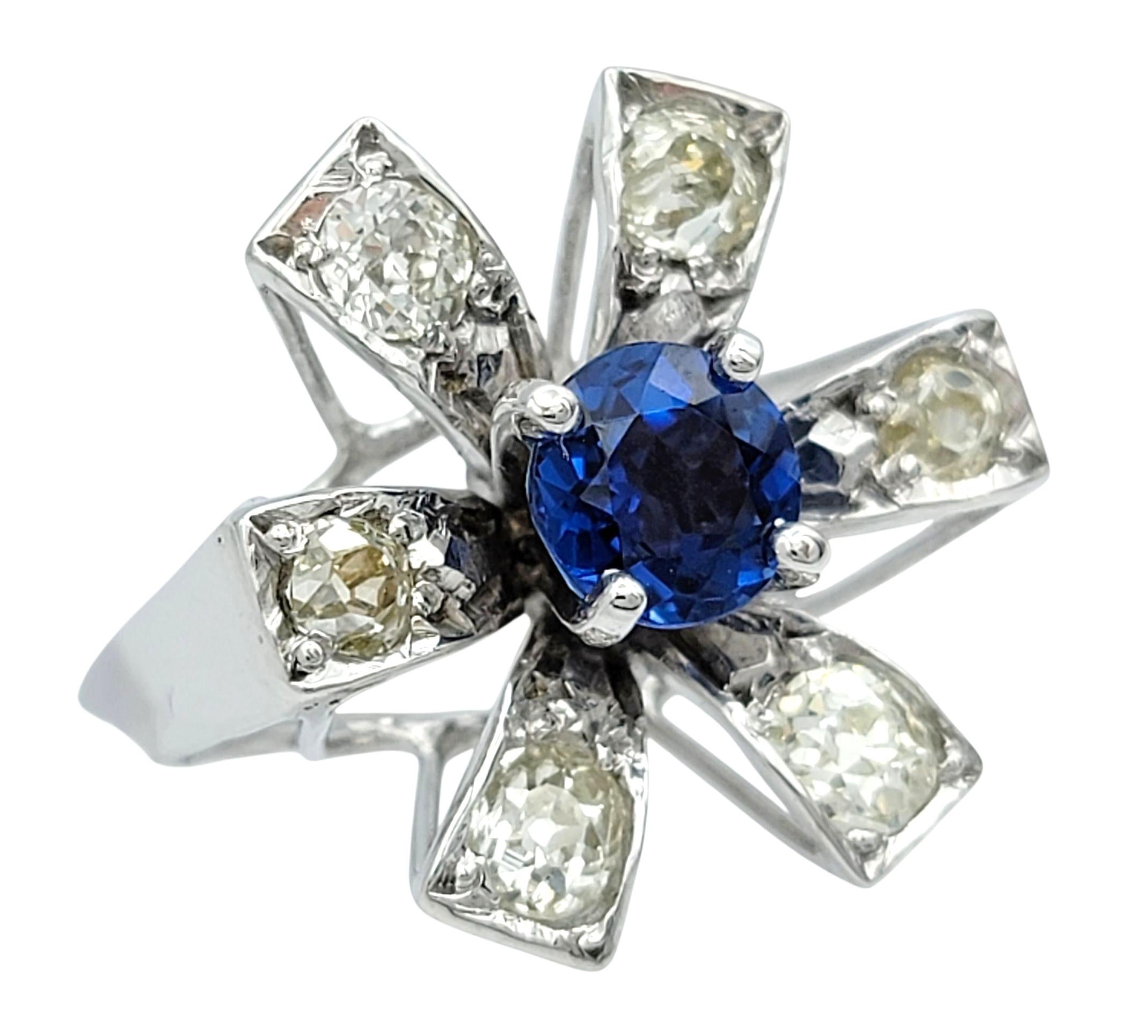 Ring size: 5.25

This vintage ring set in 10 karat white gold showcases a bold starburst design that is both sculptural and refined. At its center, a vivid round blue sapphire radiates rich color, while six Old Mine cut diamonds extend outward in a