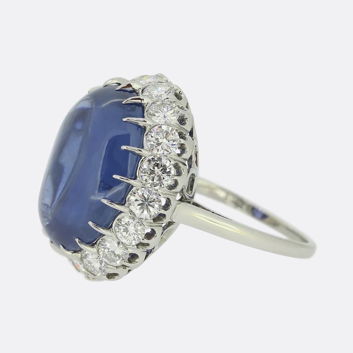 Here we have an outstanding sapphire and diamond cocktail ring. A large 19.30ct natural cabochon sapphire of Ceylon origin sits at the centre of the face and showcases a stunning violet blue colour tone. This principle stone is then framed by a