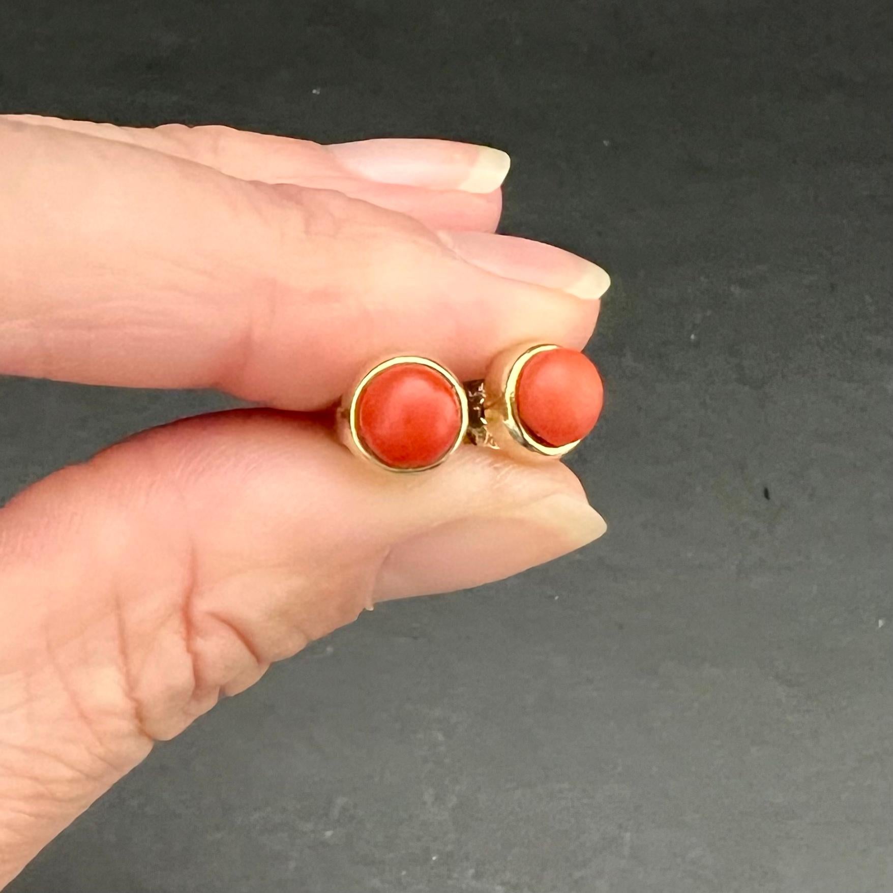 A lovely pair of vintage natural red coral and gold stud earrings. The coral studs are bezel set in a 14 karat gold mounting. The gold mounting has a smooth setting crafted around a red coral cabochon stone. The stones have a beautiful red color and